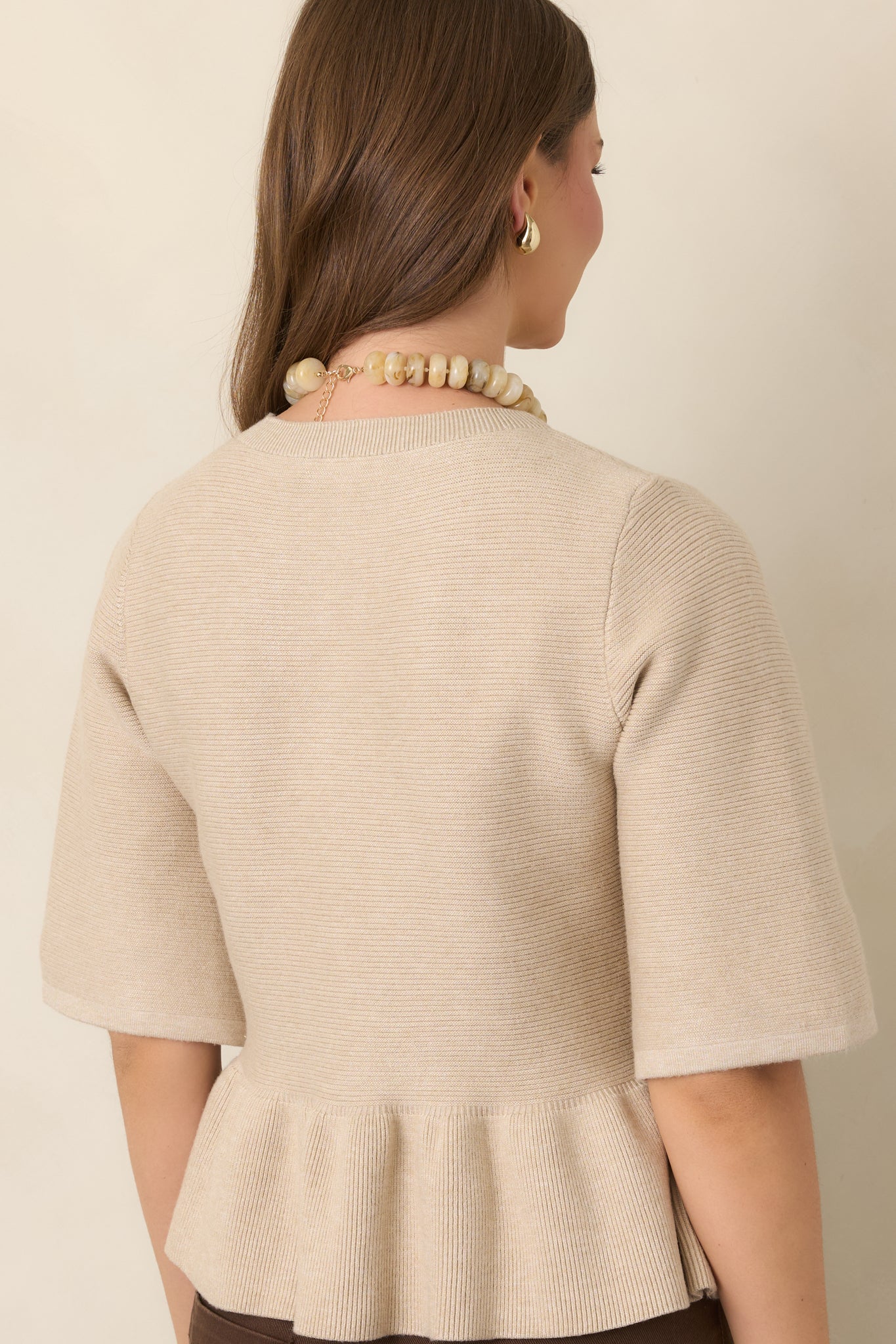 Rear view of the oatmeal knit top showcasing its fitted bodice, elbow-length sleeves, and softly gathered peplum hem.