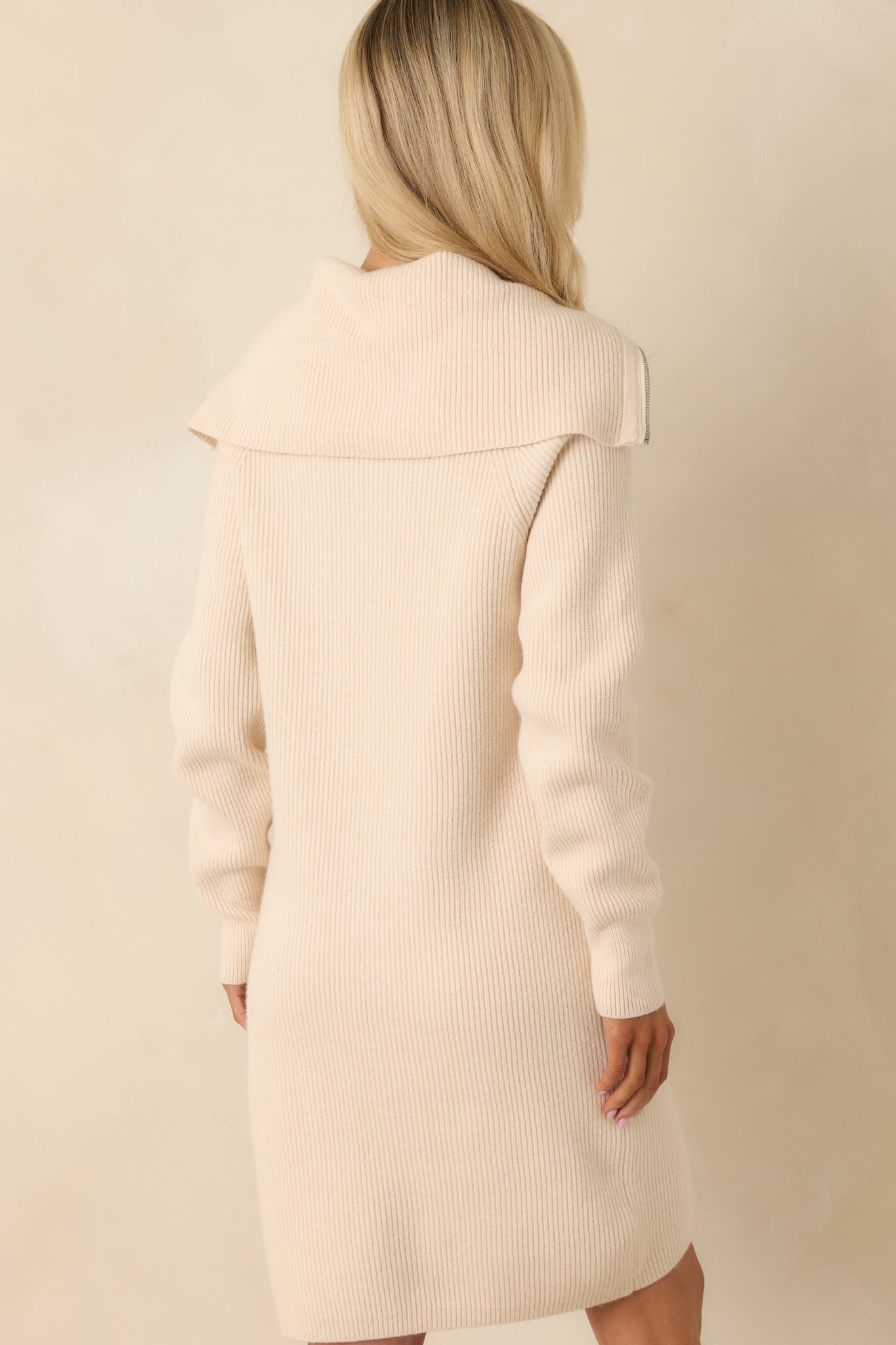 Rear view of beige sweater dress showing straight hemline and relaxed silhouette.