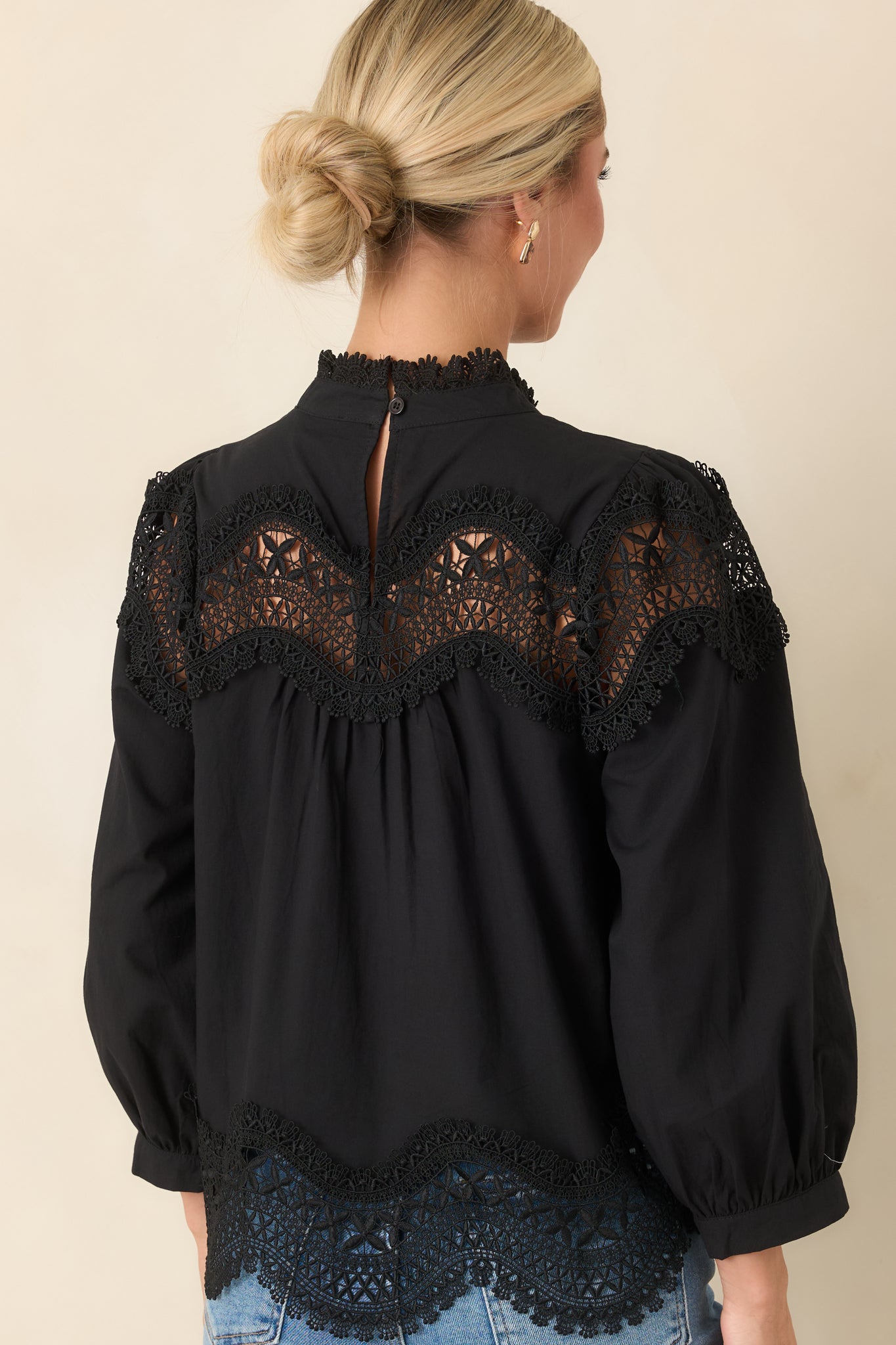 Rear view of the black blouse showcasing the keyhole button closure and lace-trimmed hem.