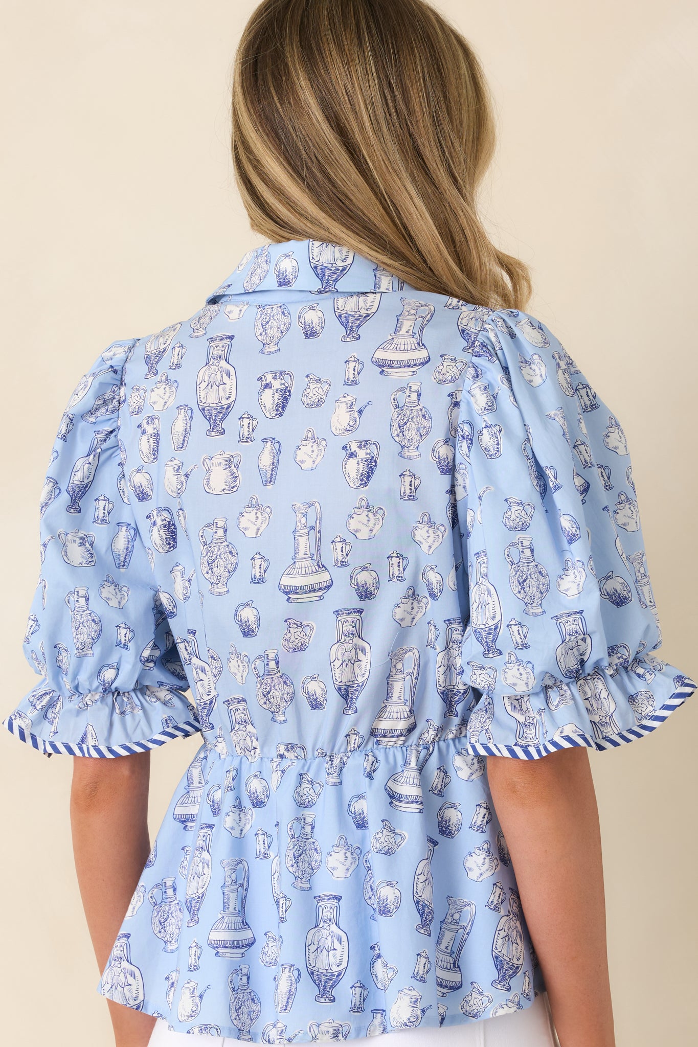 Rear view of soft blue top with puff sleeves, structured collar, and toile pattern.