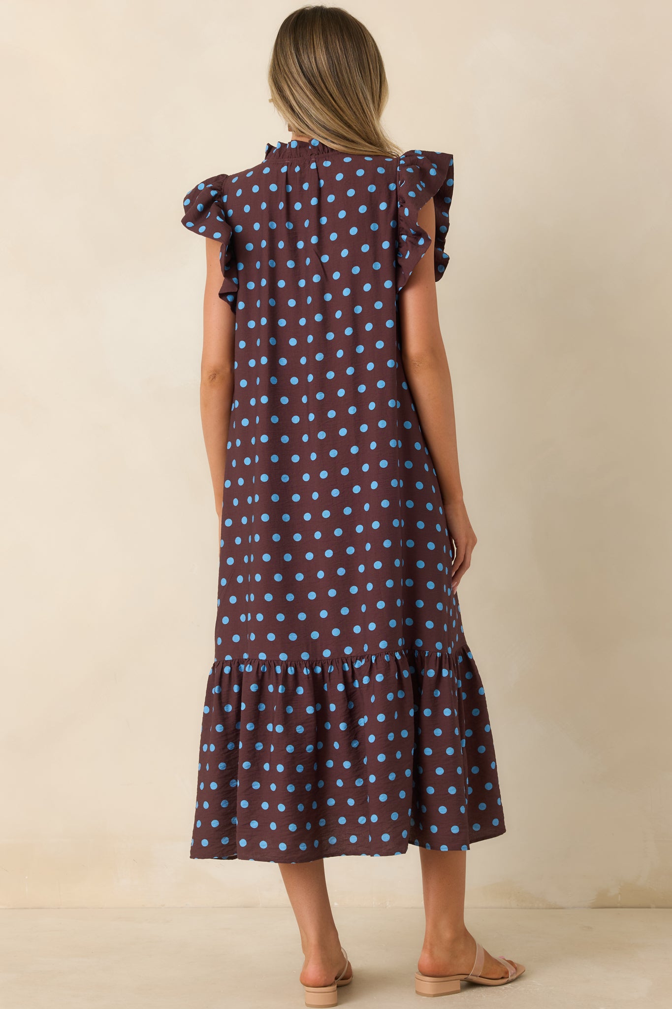 Rear view of the brown polka dot midi dress showcasing the flowing silhouette, flutter sleeves, and tiered hem.