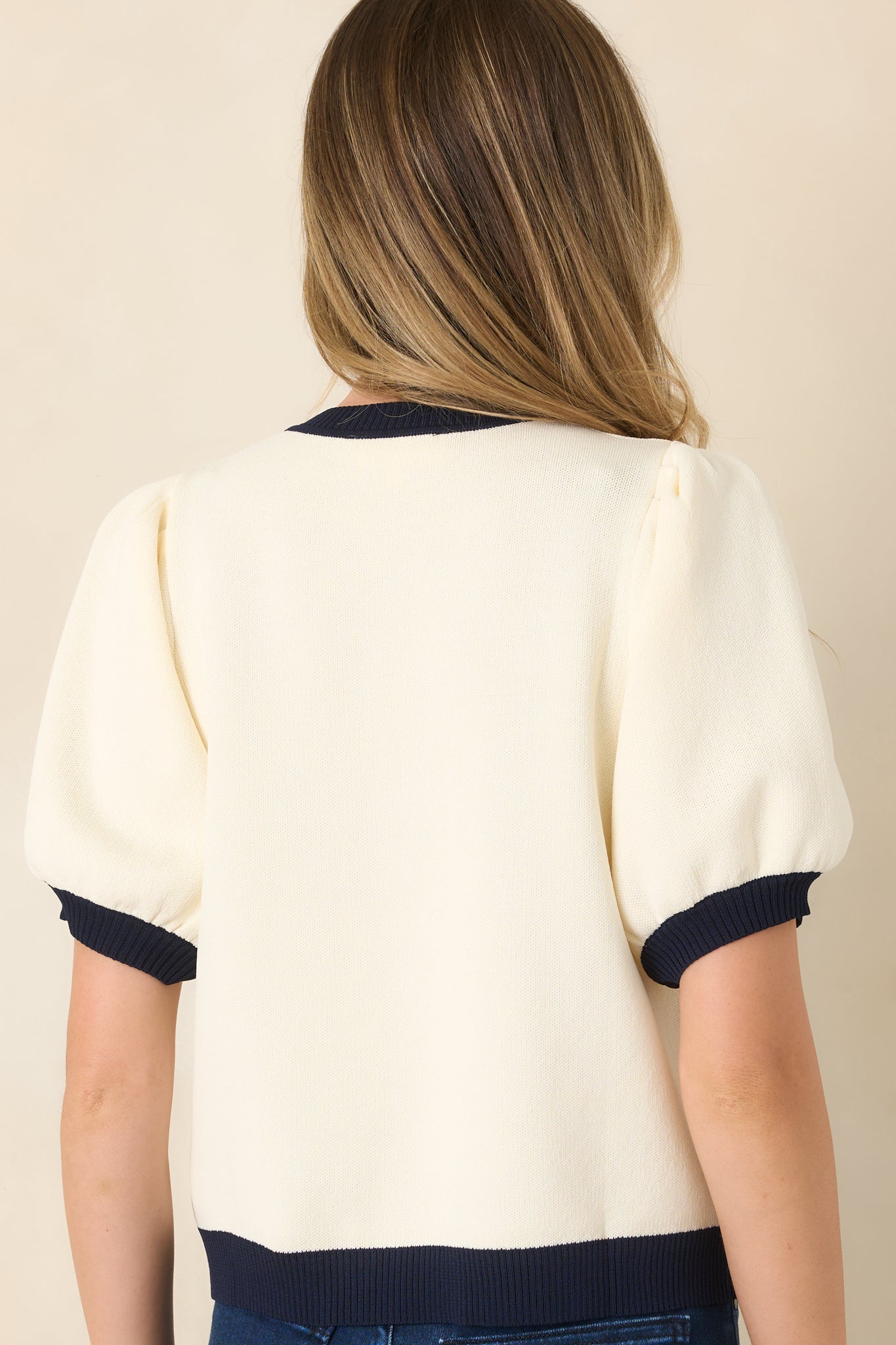 Rear view of the ivory knit top showcasing the contrast navy hem and relaxed silhouette.