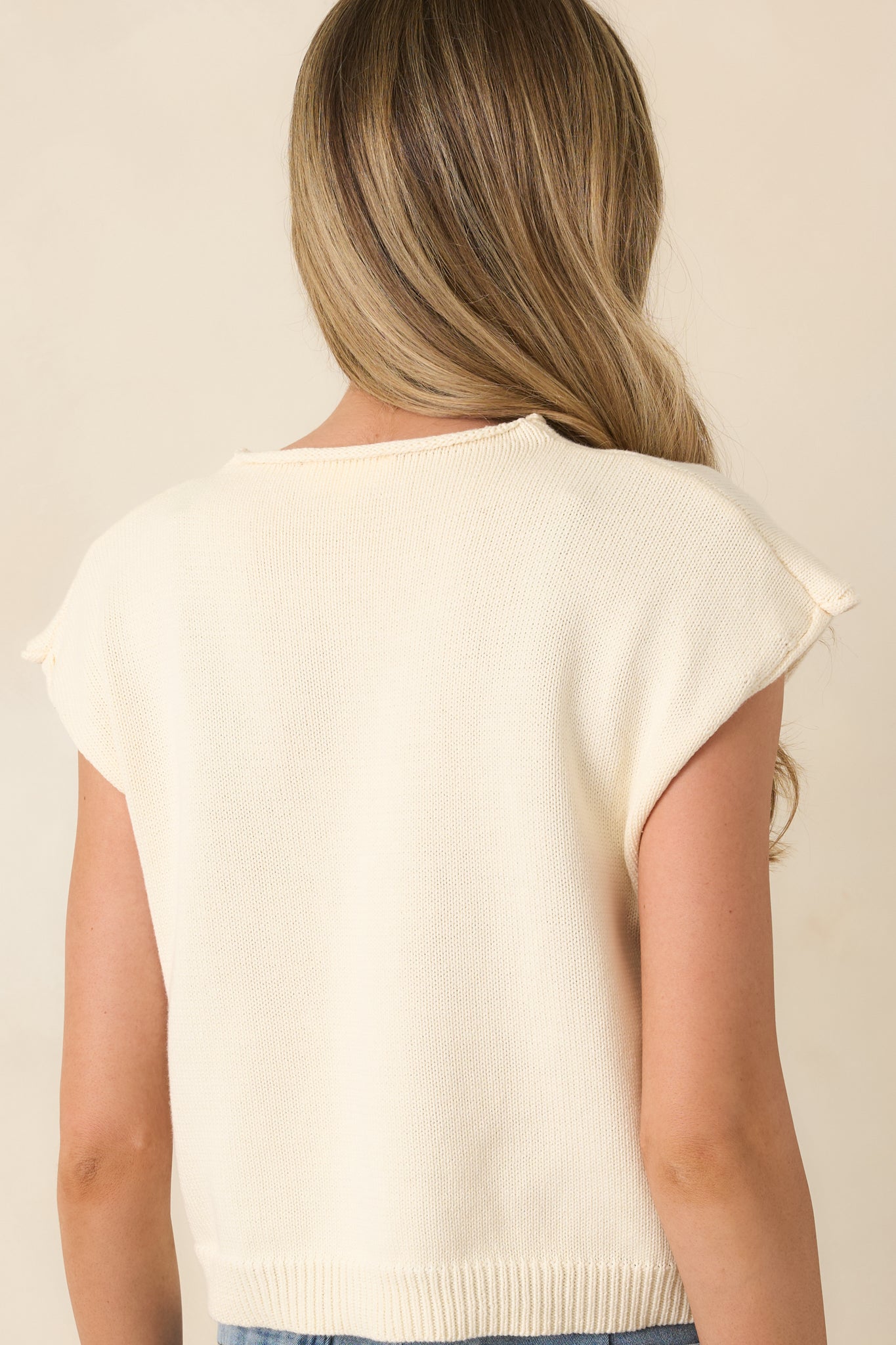 Rear view of ivory sleeveless knit top showing smooth, relaxed fit and cap shoulders.