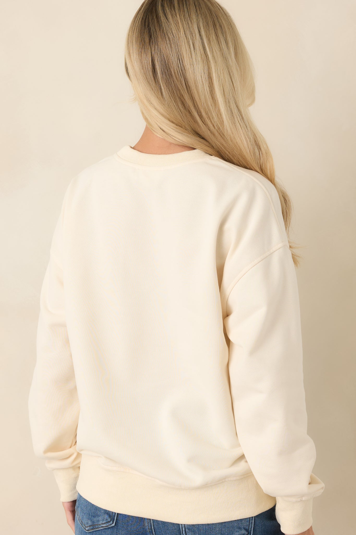 Rear view of the ivory sweatshirt showcasing the clean back design, long sleeves, and ribbed hem.