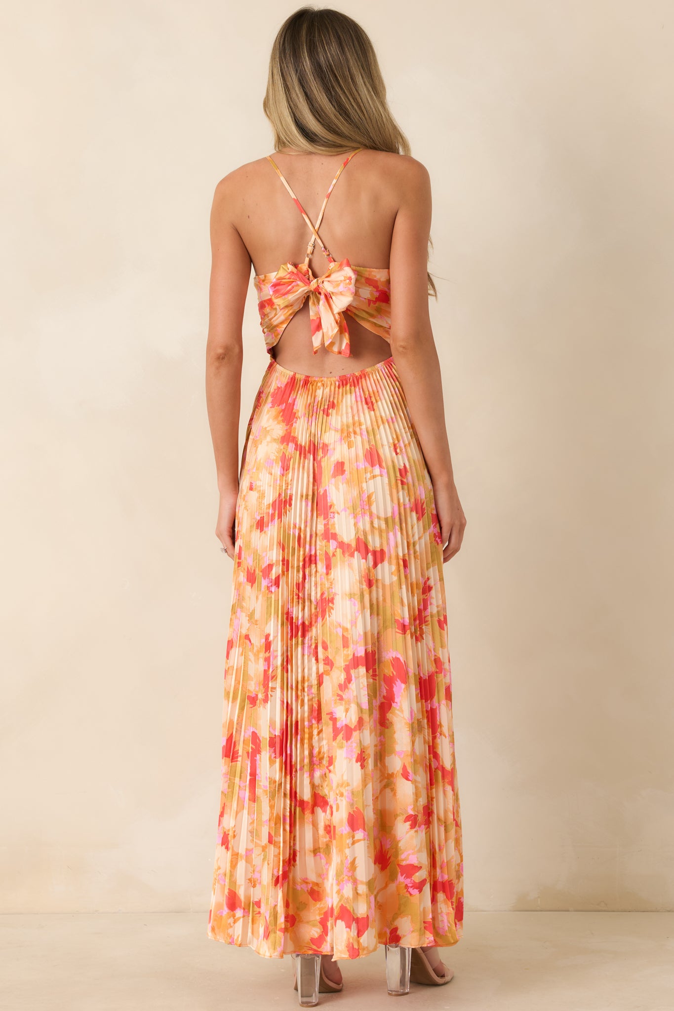 Rear view of maxi dress featuring open back with halter tie straps and statement bow detail.

