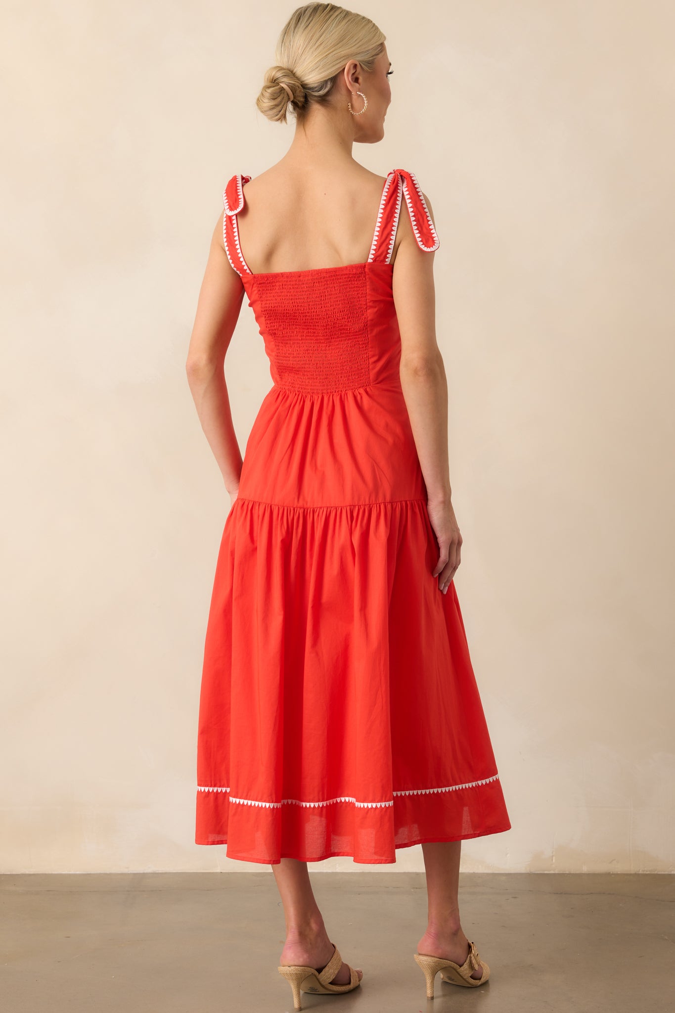 Rear view of the dress showing the smocked back panel, bow-tied shoulder straps, and the continuation of the embroidered trim around the upper back.