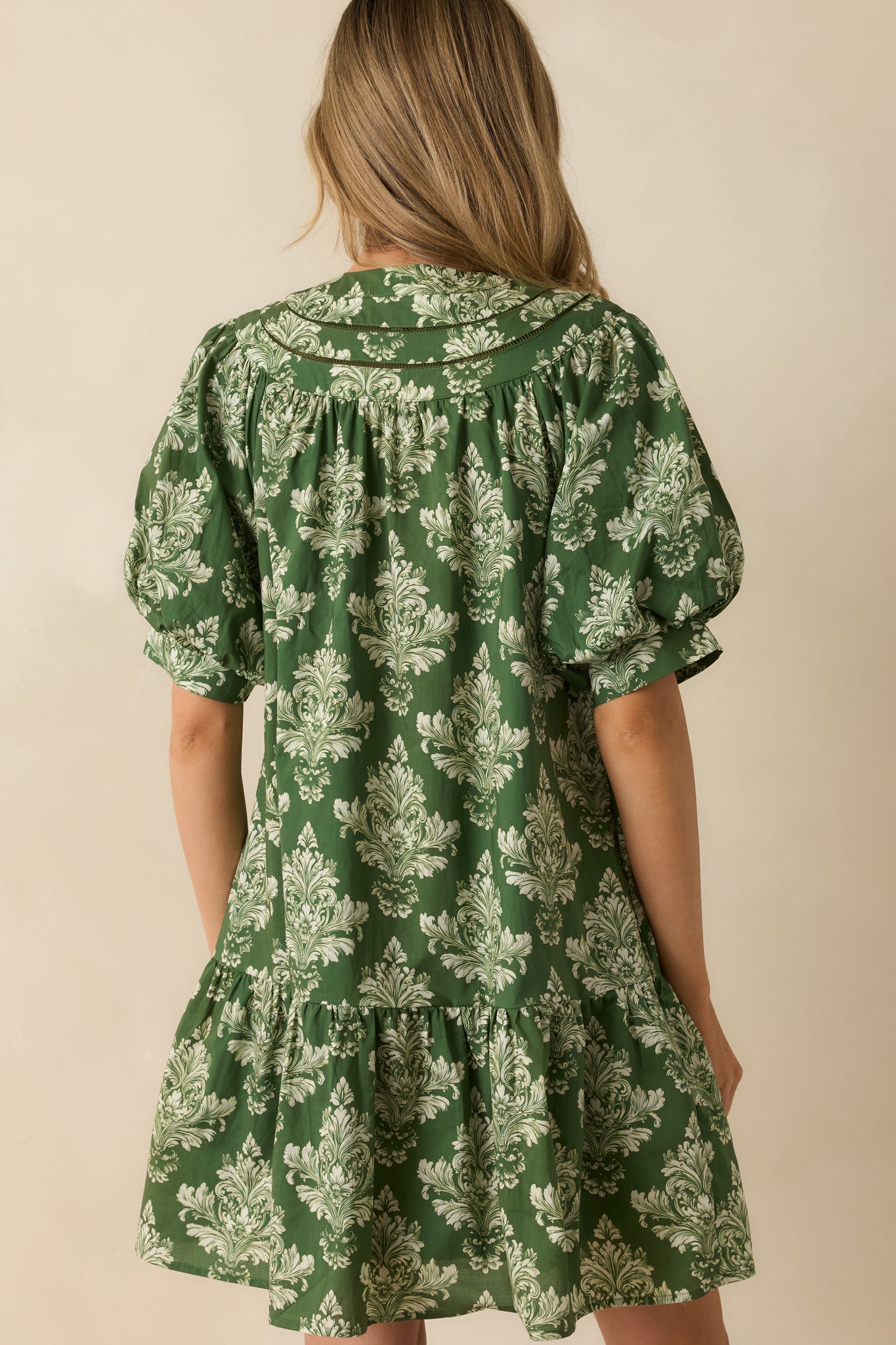 Rear view of the green and ivory damask mini dress showing short puff sleeves, elastic cuffs, and tiered hem.