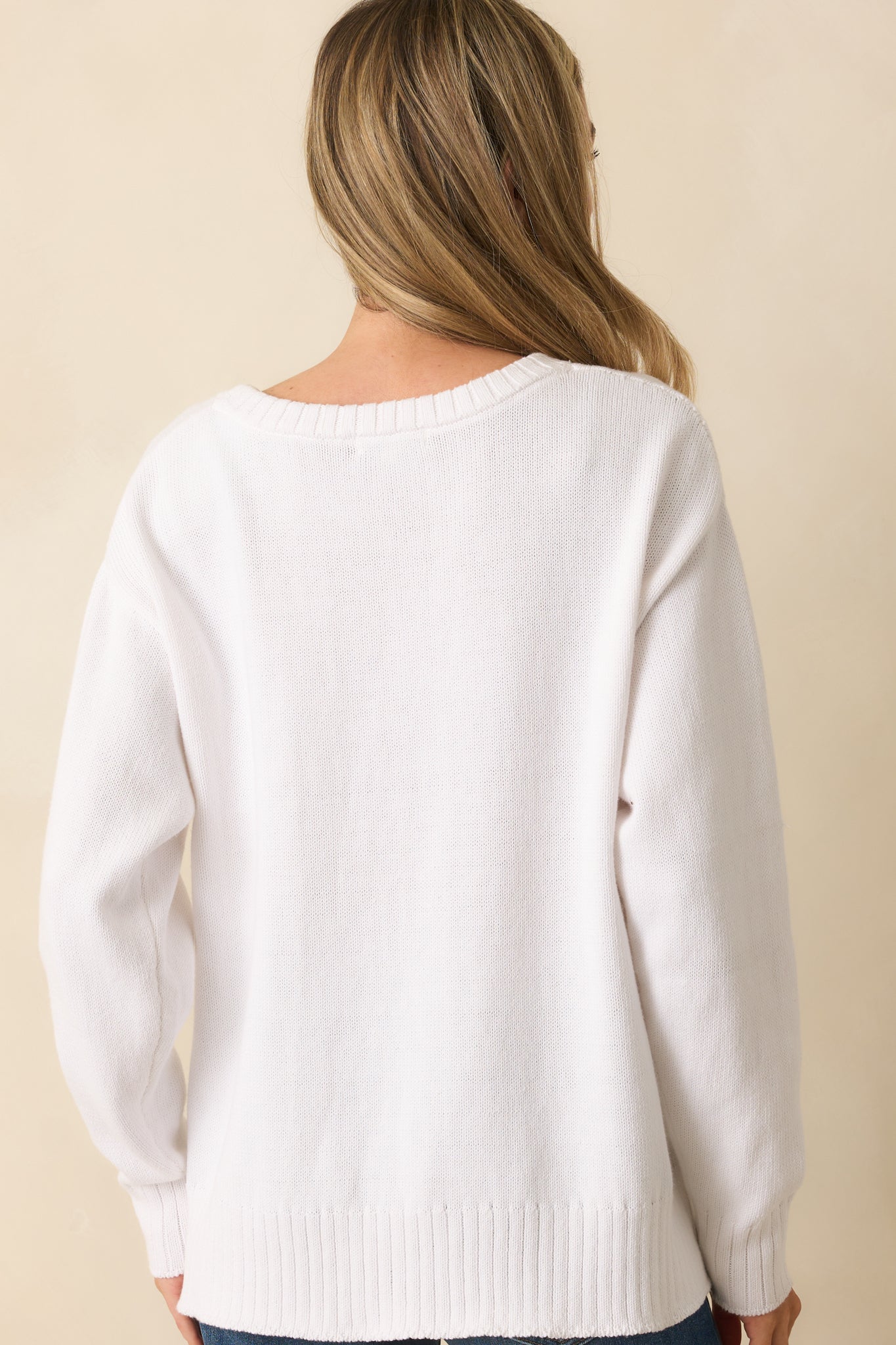 Rear view of white knit sweater showing relaxed fit, drop shoulder sleeves, and ribbed hem.