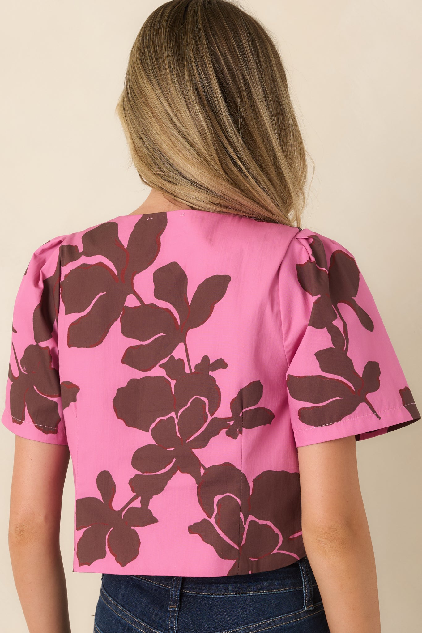 Rear view of the bright pink top featuring the oversized chocolate brown floral print, round neckline, short puff sleeves, and softly structured silhouette.