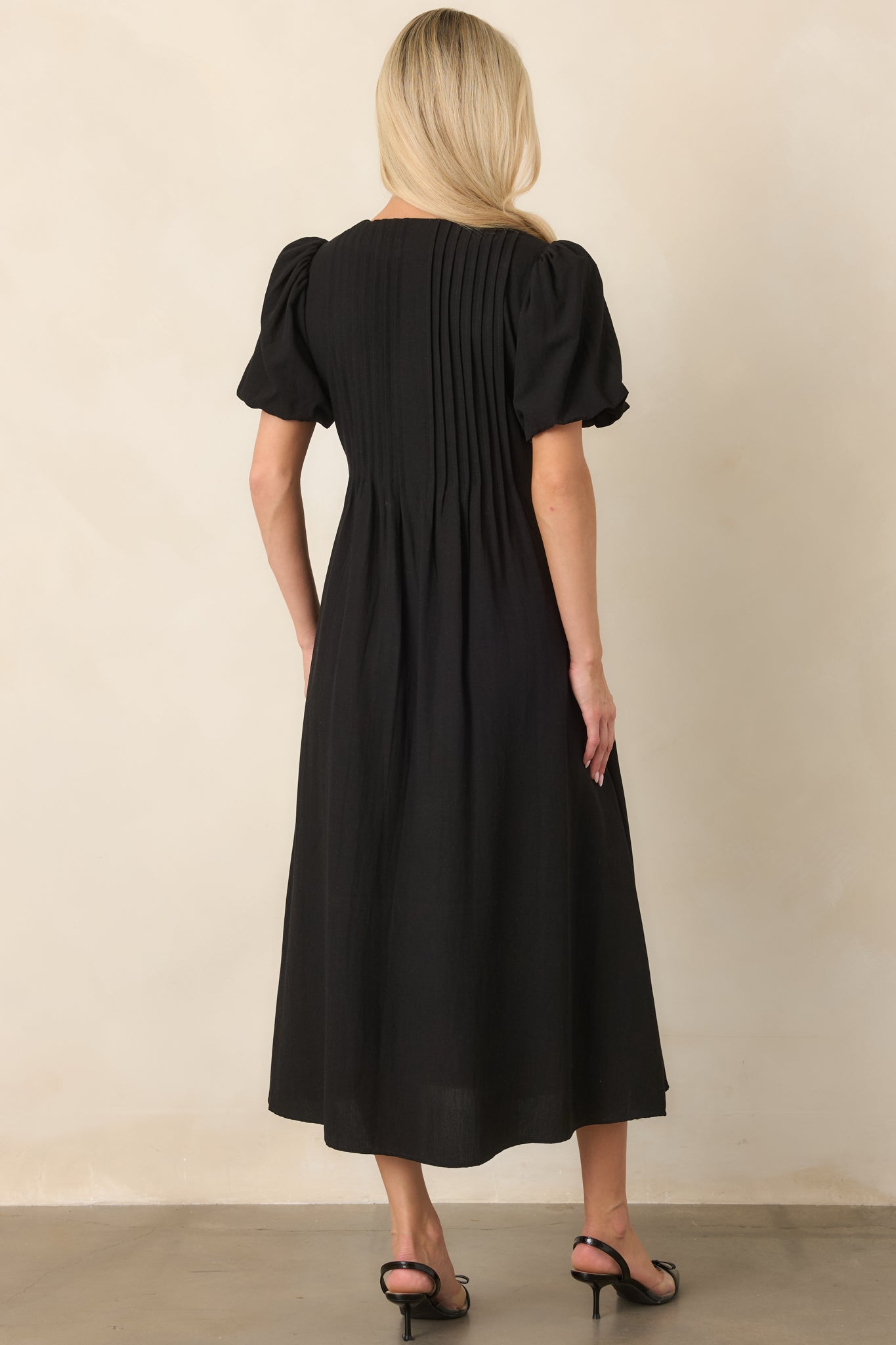 Rear view of the rayon-nylon midi dress showing pintuck detailing across the back, gathered sleeves, flowing skirt, and clean silhouette.