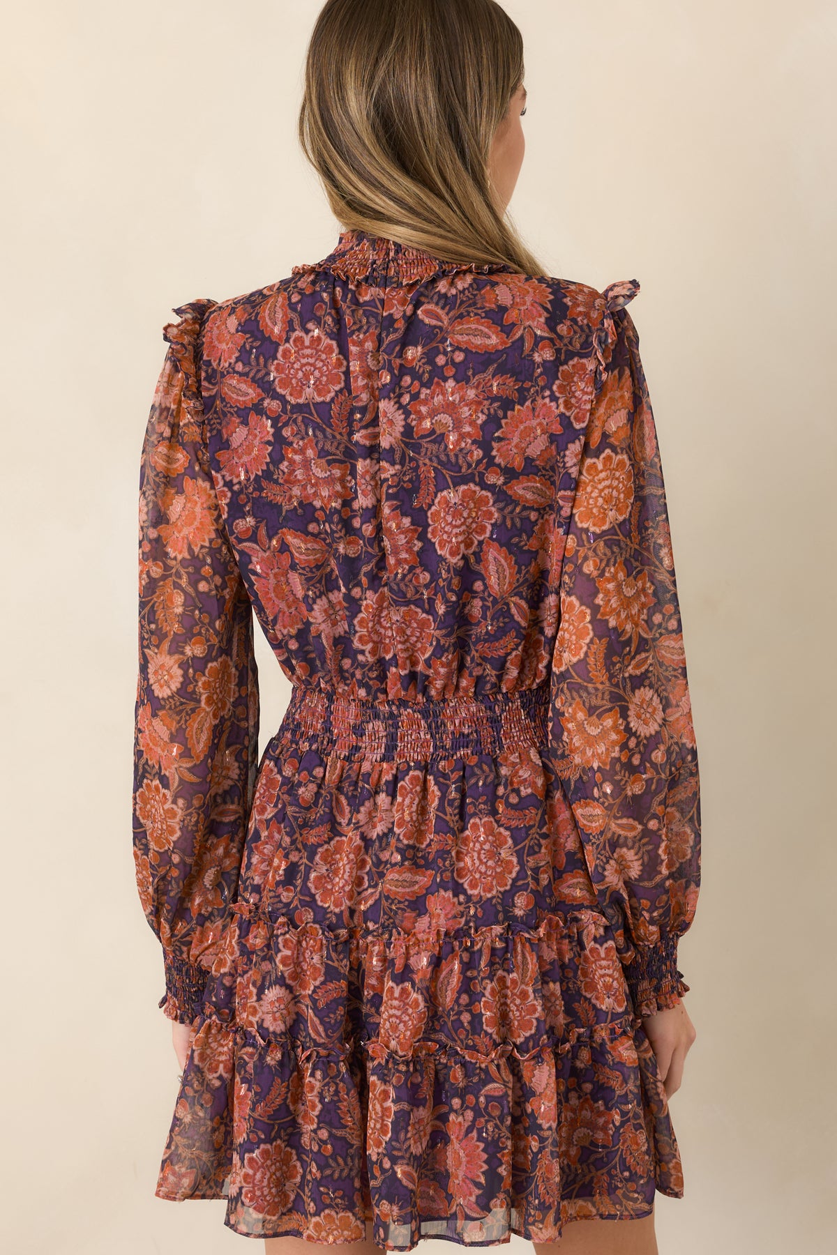Rear view of the deep plum floral mini dress featuring a wide smocked waist, sheer sleeves, and tiered skirt.