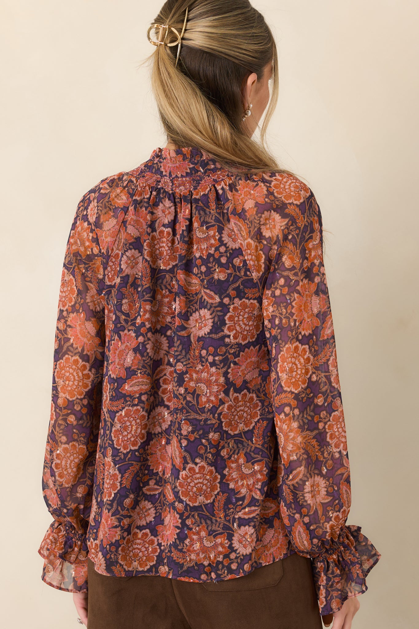 Rear view of the sheer plum floral top showcasing its lightweight overlay, long sleeves, and ruffled cuffs.