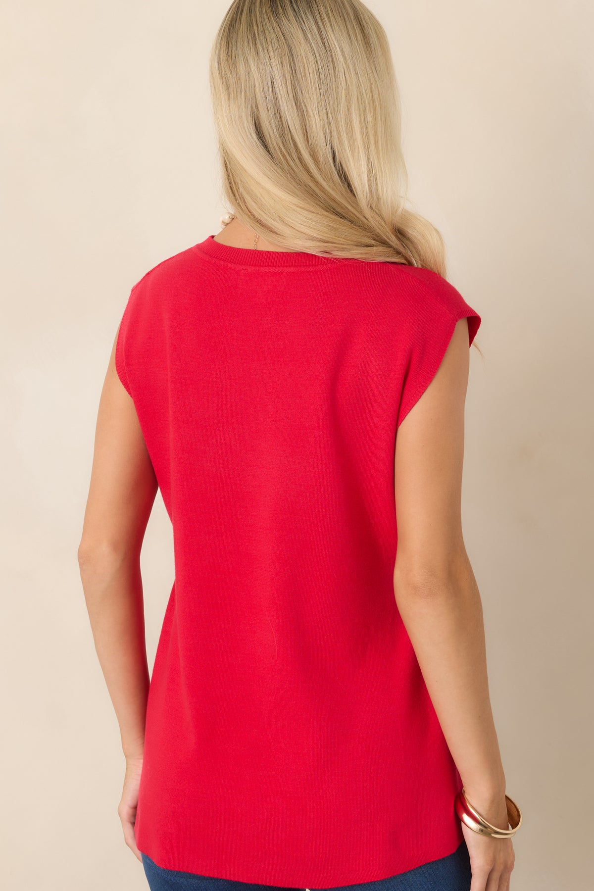 Rear view of the red knit top showcasing its draped high-low silhouette, cap sleeves, round neckline, and smooth lightweight fabric.