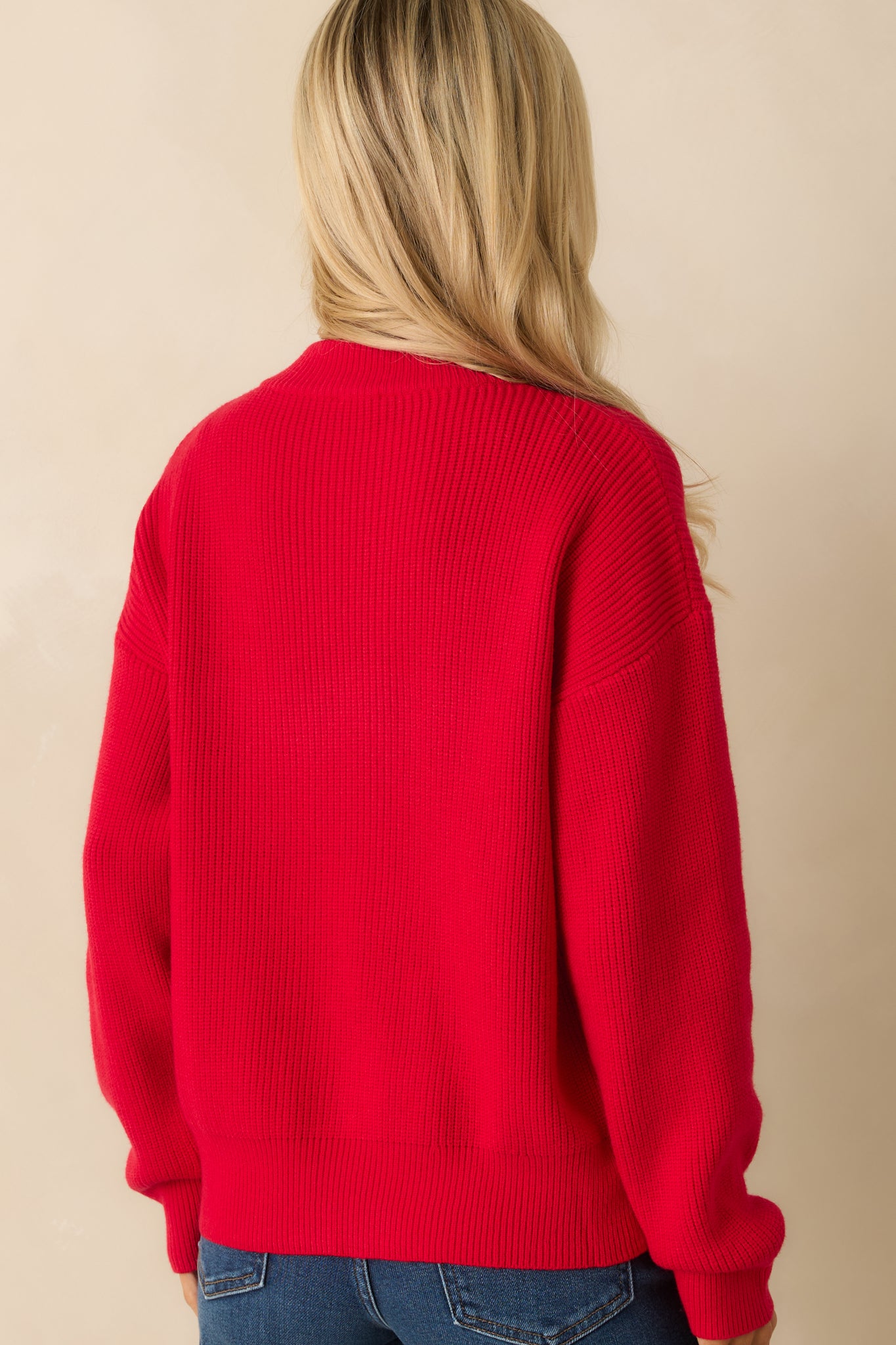 Rear view of red knit pullover sweater showing dropped shoulders, ribbed hem, and relaxed fit.