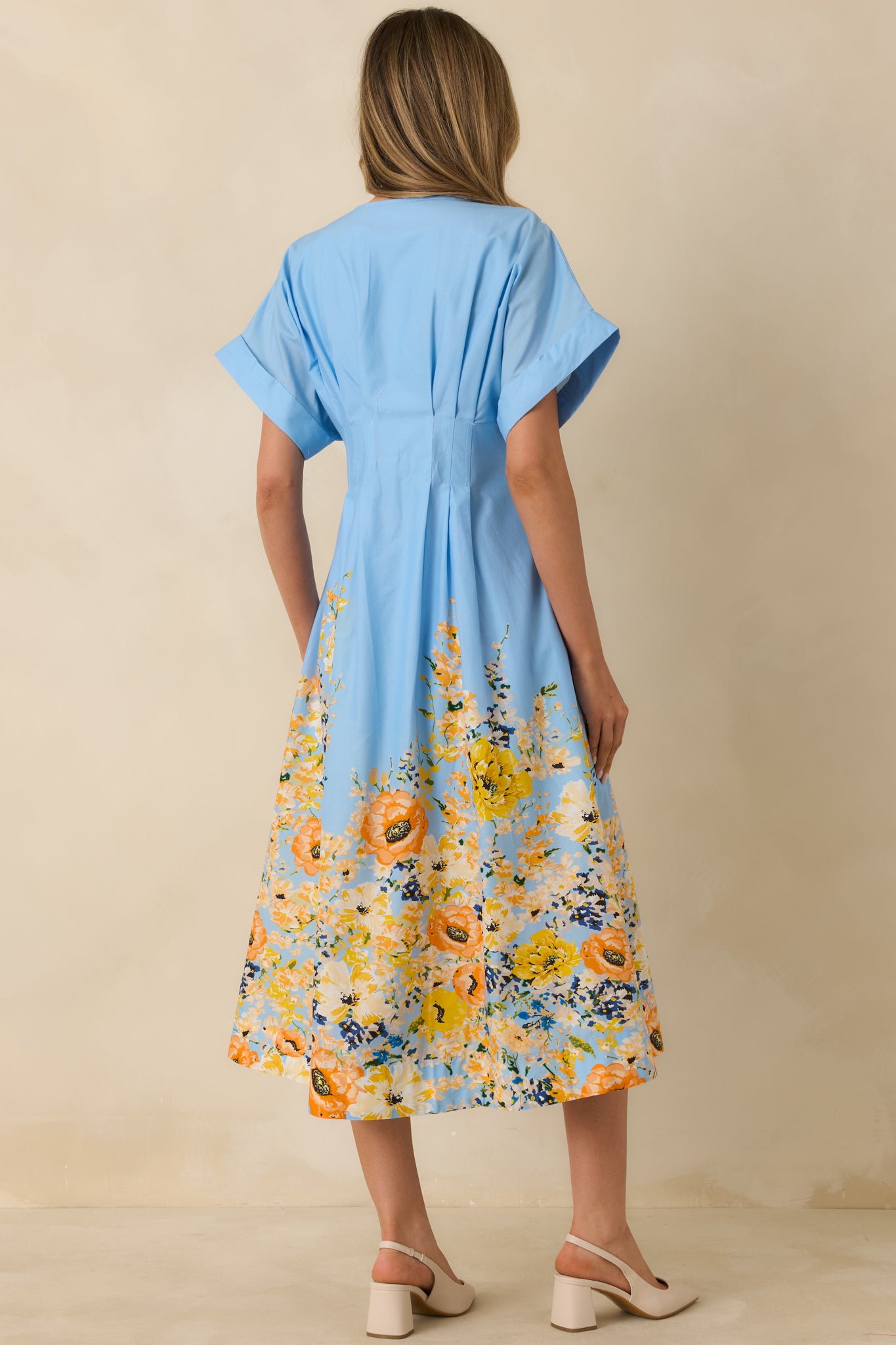 Rear view of blue midi dress revealing smooth back, flutter sleeves, and flowy hemline with floral border accent.