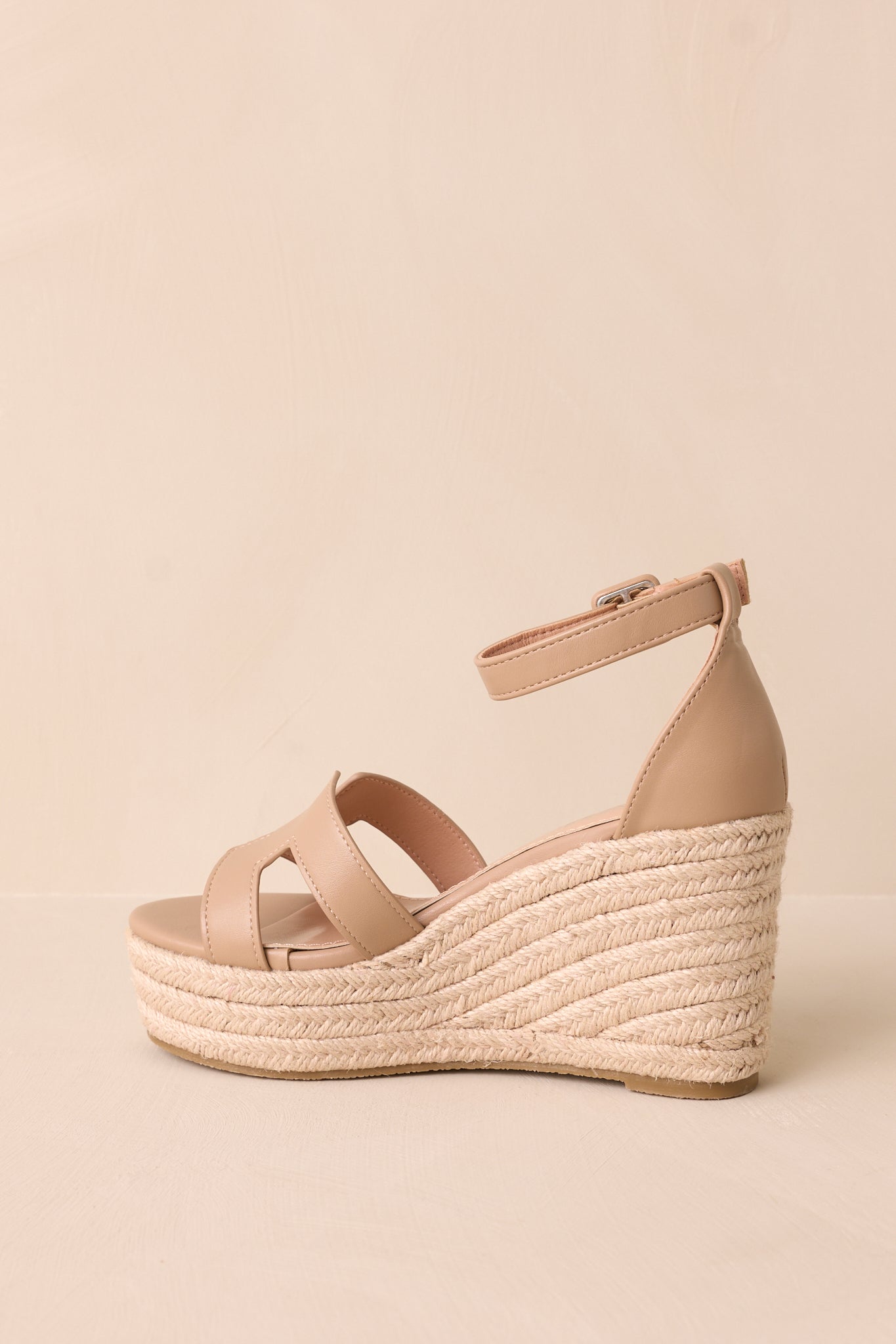 A rear view of the wedges, showcasing the full height of the beige woven straw wedge heel and the tan ankle strap wrapping around the back.