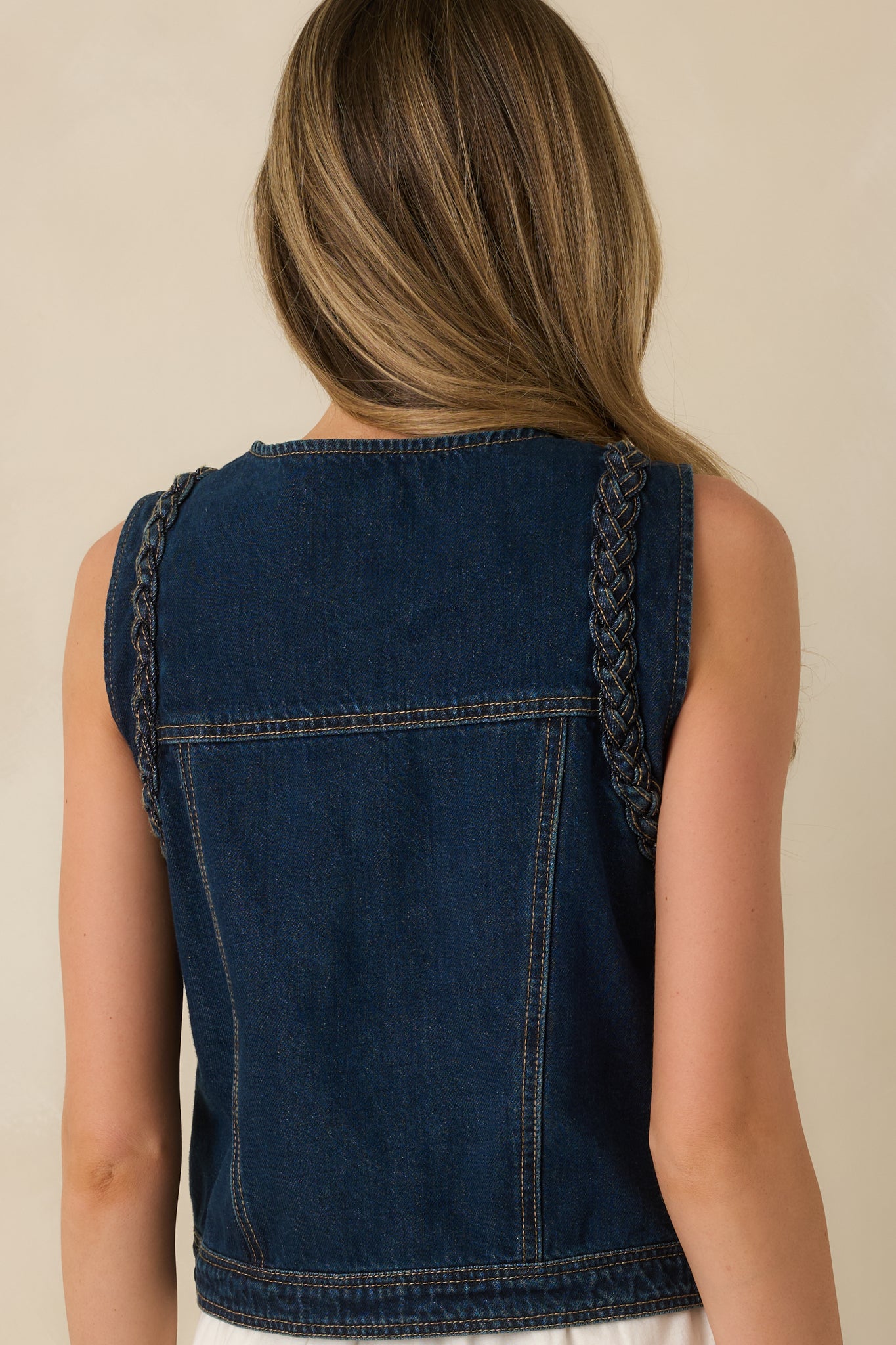 Rear view of dark wash denim vest showing smooth back fabric and braided trim along shoulder seams.