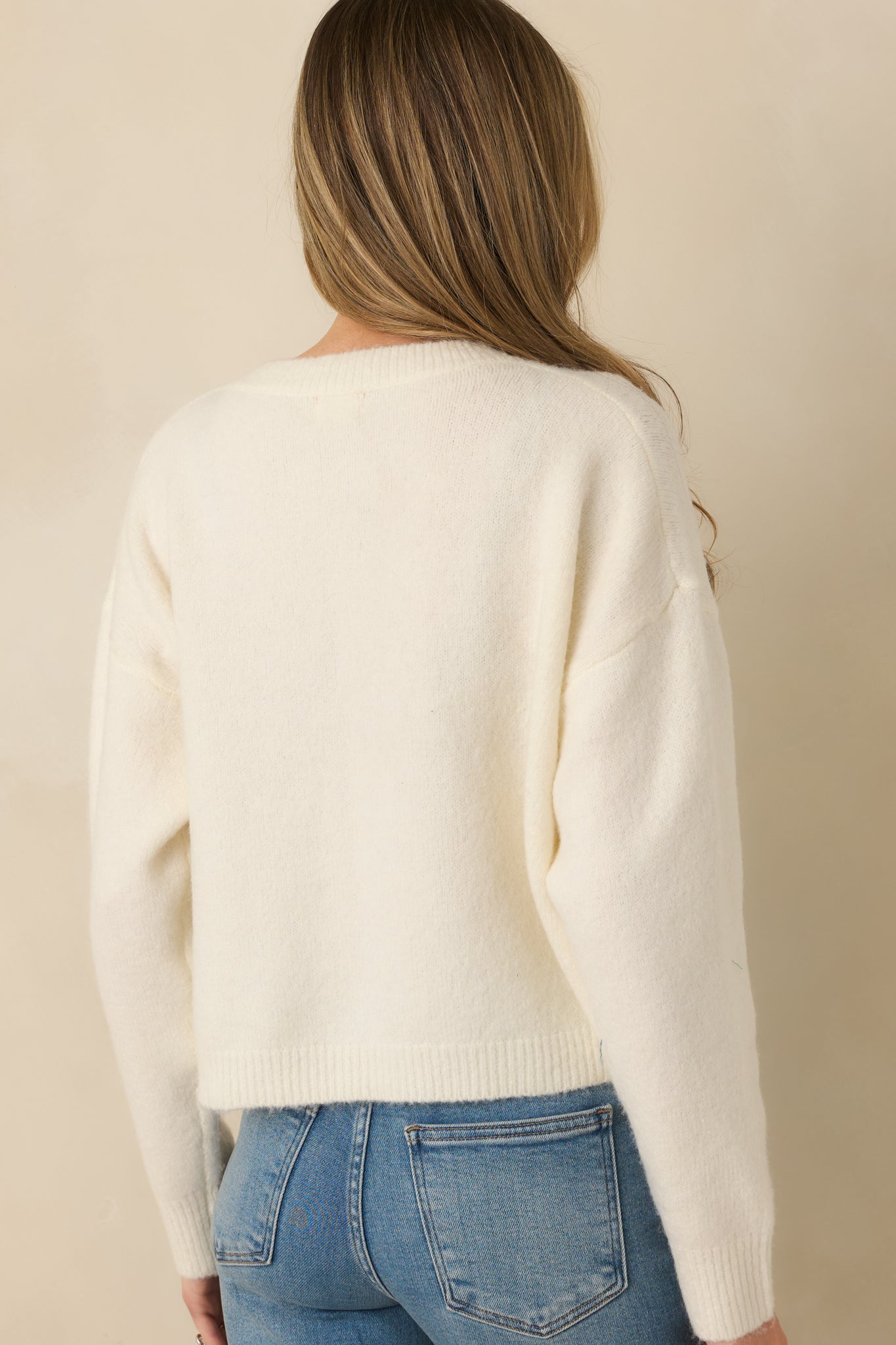 Rear view of ivory knit cardigan showing smooth knit fabric, long sleeves, and slightly cropped fit.