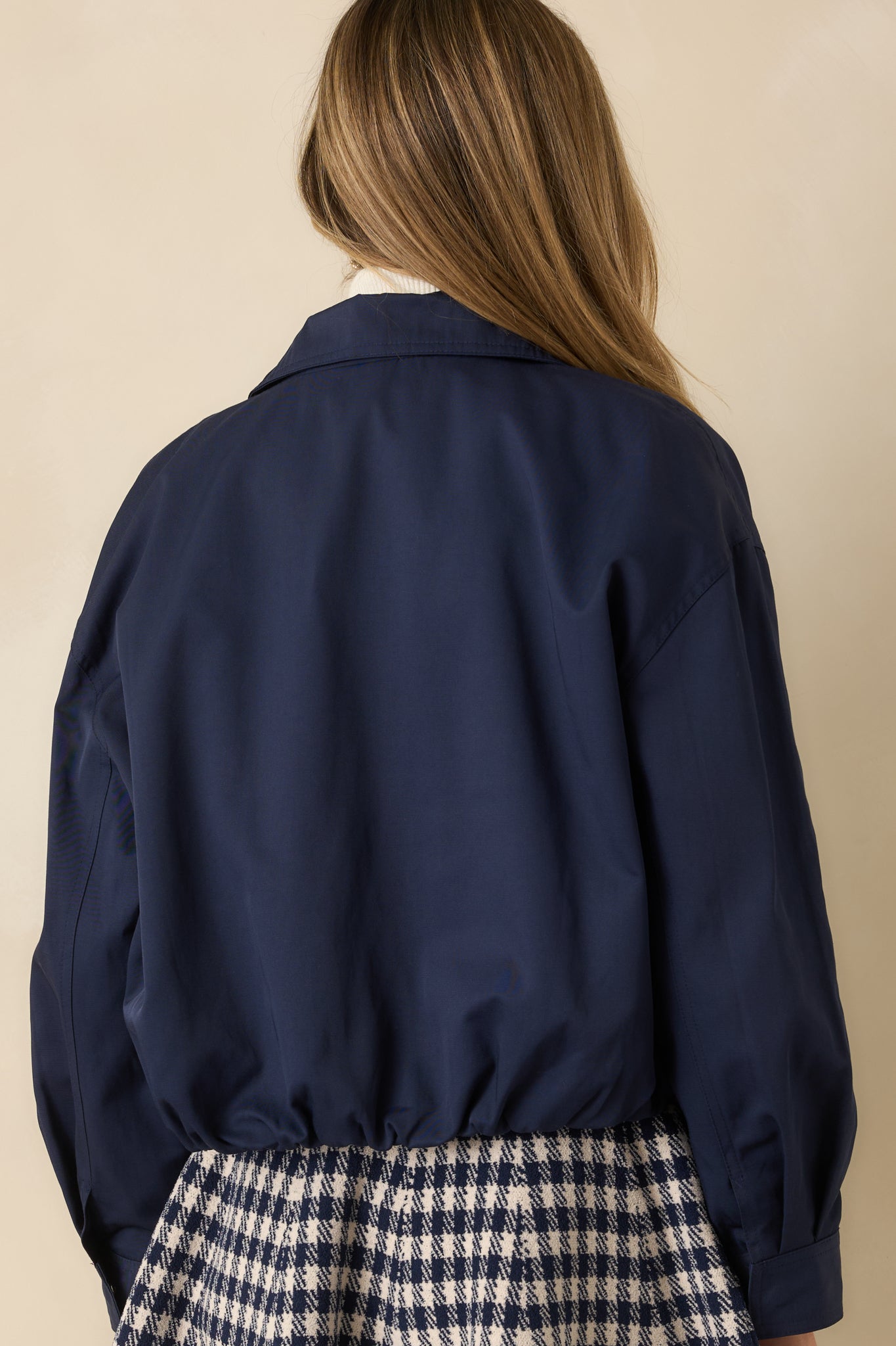Rear view of navy bomber jacket showing elasticized back hem, long sleeves, and relaxed fit.