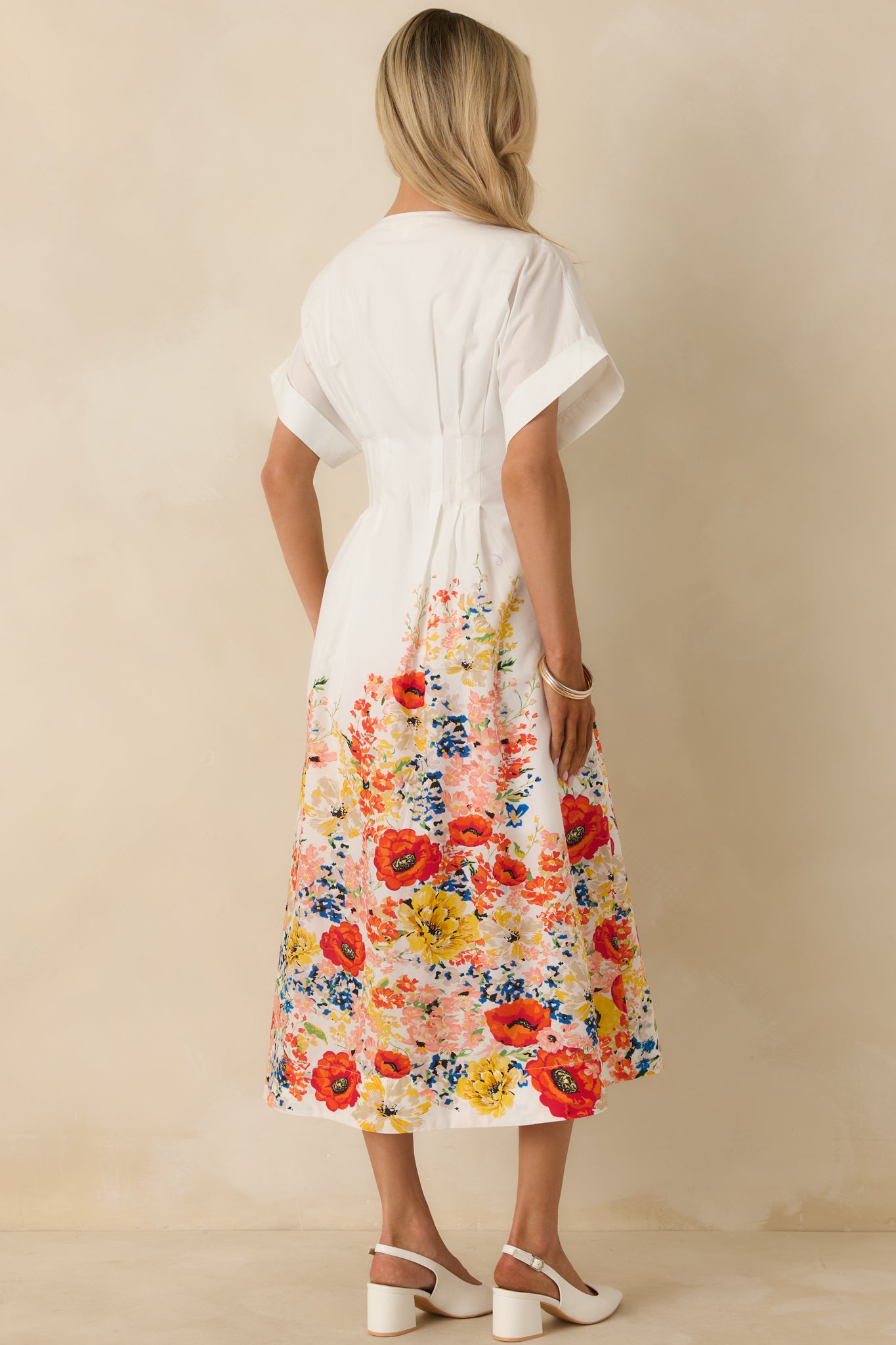 Rear view of the white cotton midi dress showing the flowy skirt, defined waist seam, and continuous floral border print at the hem.