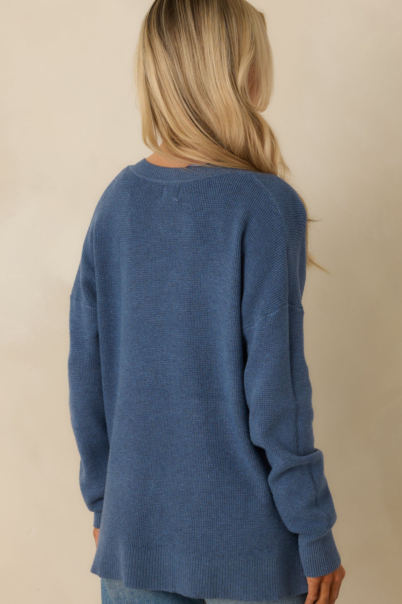 Rear view of the blue sweater showing the relaxed fit, long sleeves, and split hem design.