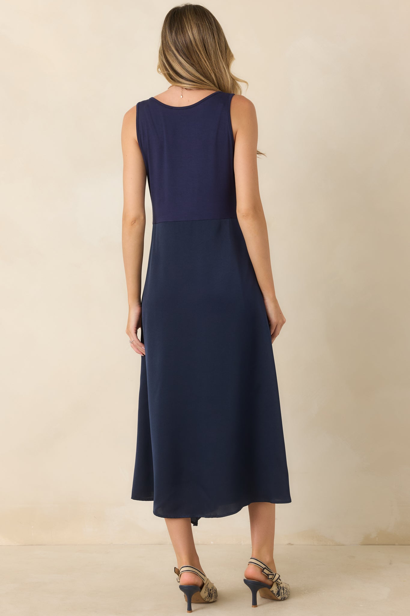 Rear view of the sleeveless midi dress featuring a smooth stretch-knit bodice, flowing satin skirt, and clean, elegant silhouette.