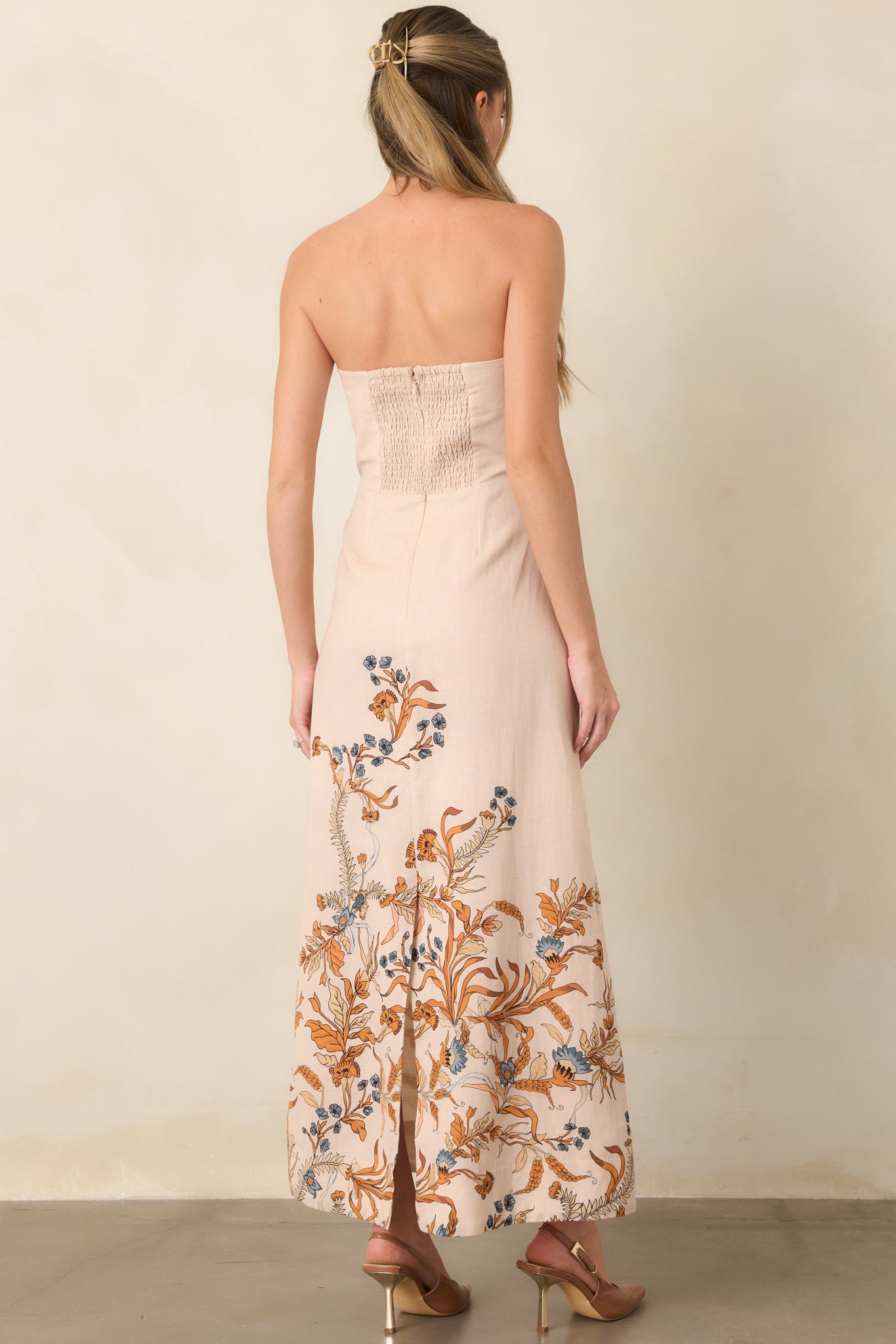 Rear view of the cotton-linen column dress showing the smocked back, fitted waist, and long skirt with floral hem accents.
