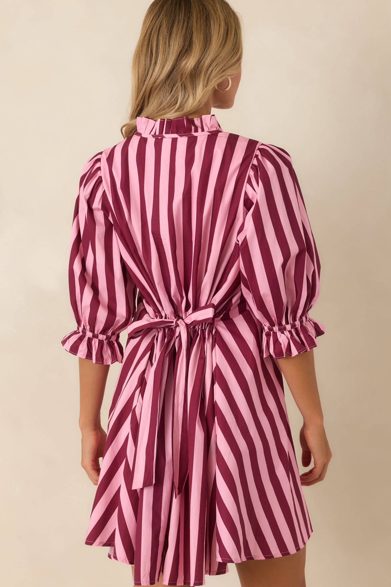 Rear view of the striped cotton mini dress featuring an adjustable tie-back waist, puff sleeves, ruffle cuffs, and relaxed shape.