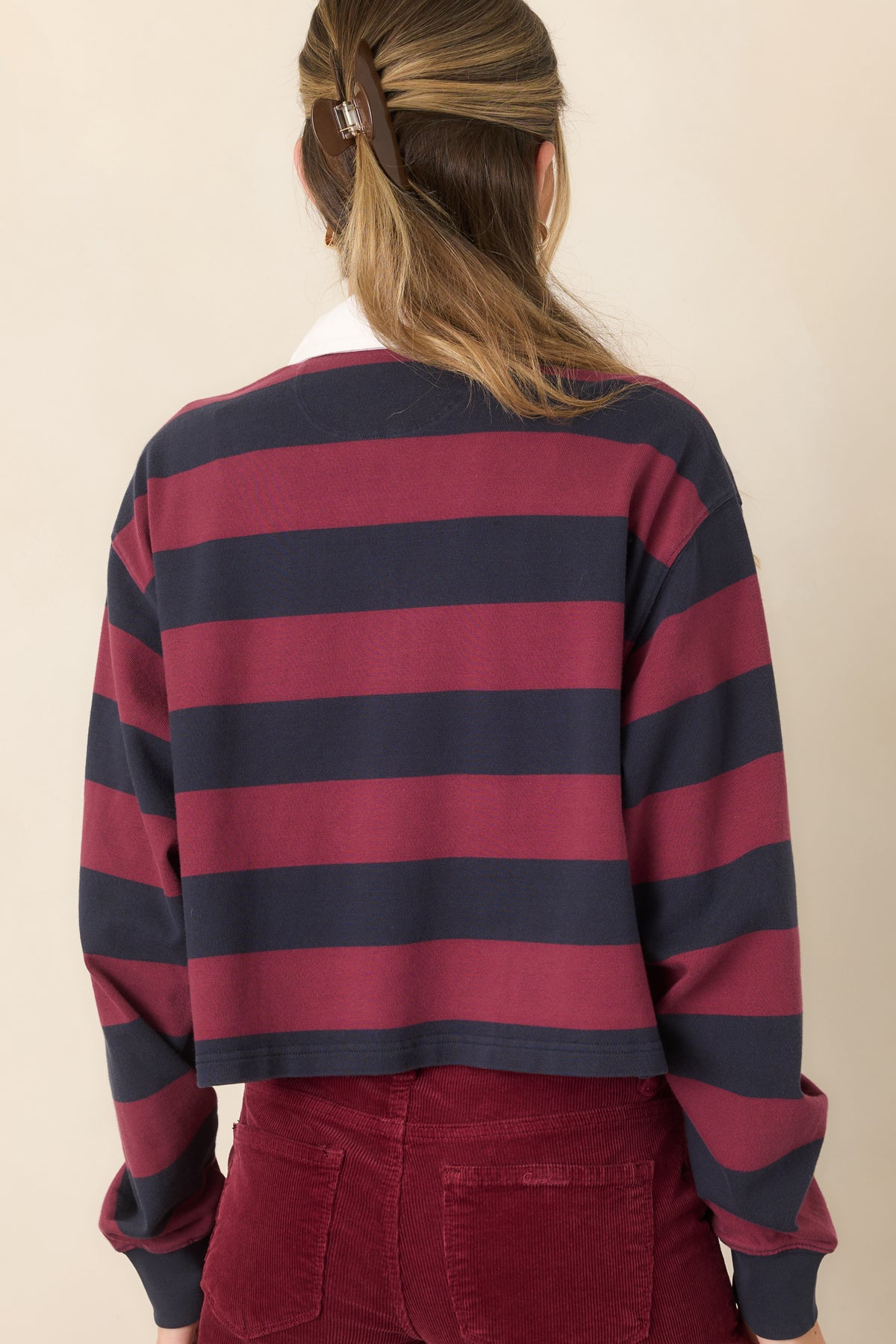 Rear of the cropped rugby polo top showing wide horizontal stripes, relaxed long sleeves, shoulders, and a straight hem.