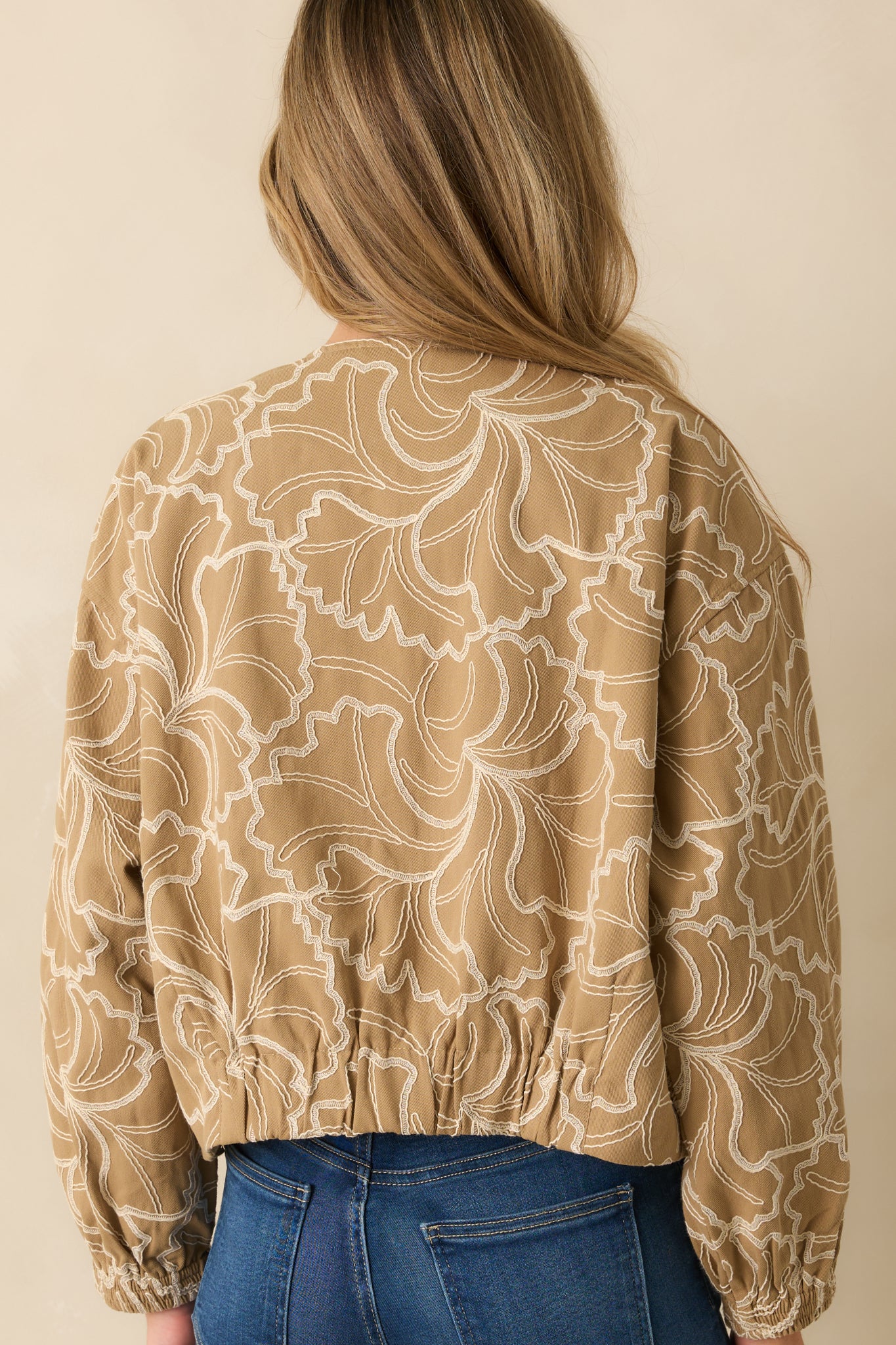 Rear view of the tan jacket featuring smooth cotton texture and ivory embroidery accents across the back.
