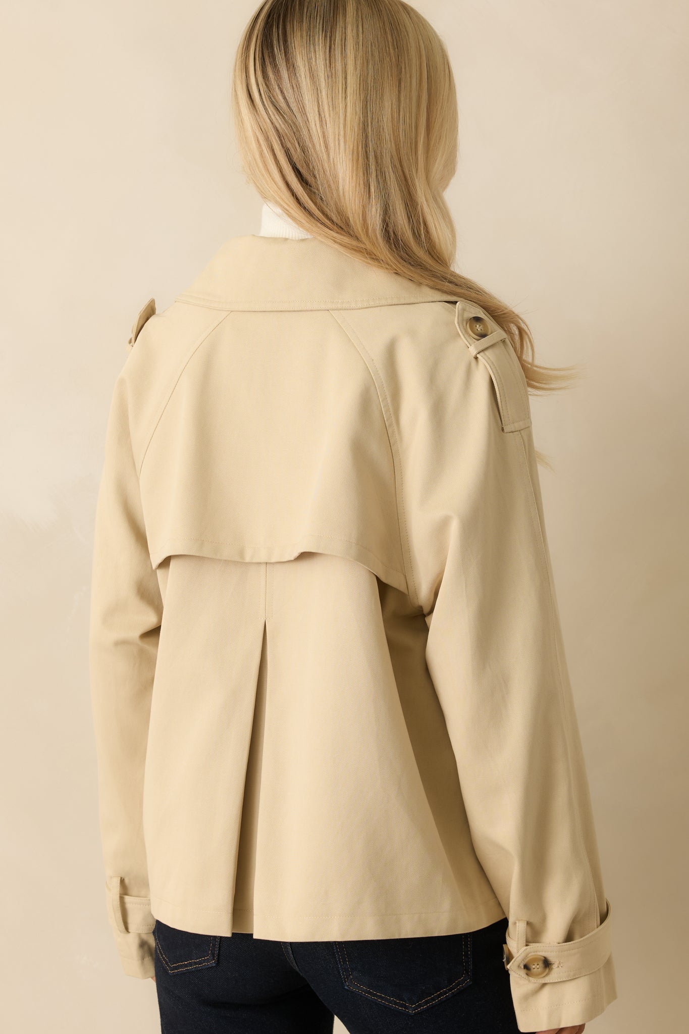 Rear view of tan trench-style jacket showing back storm flap with box pleat and relaxed fit.