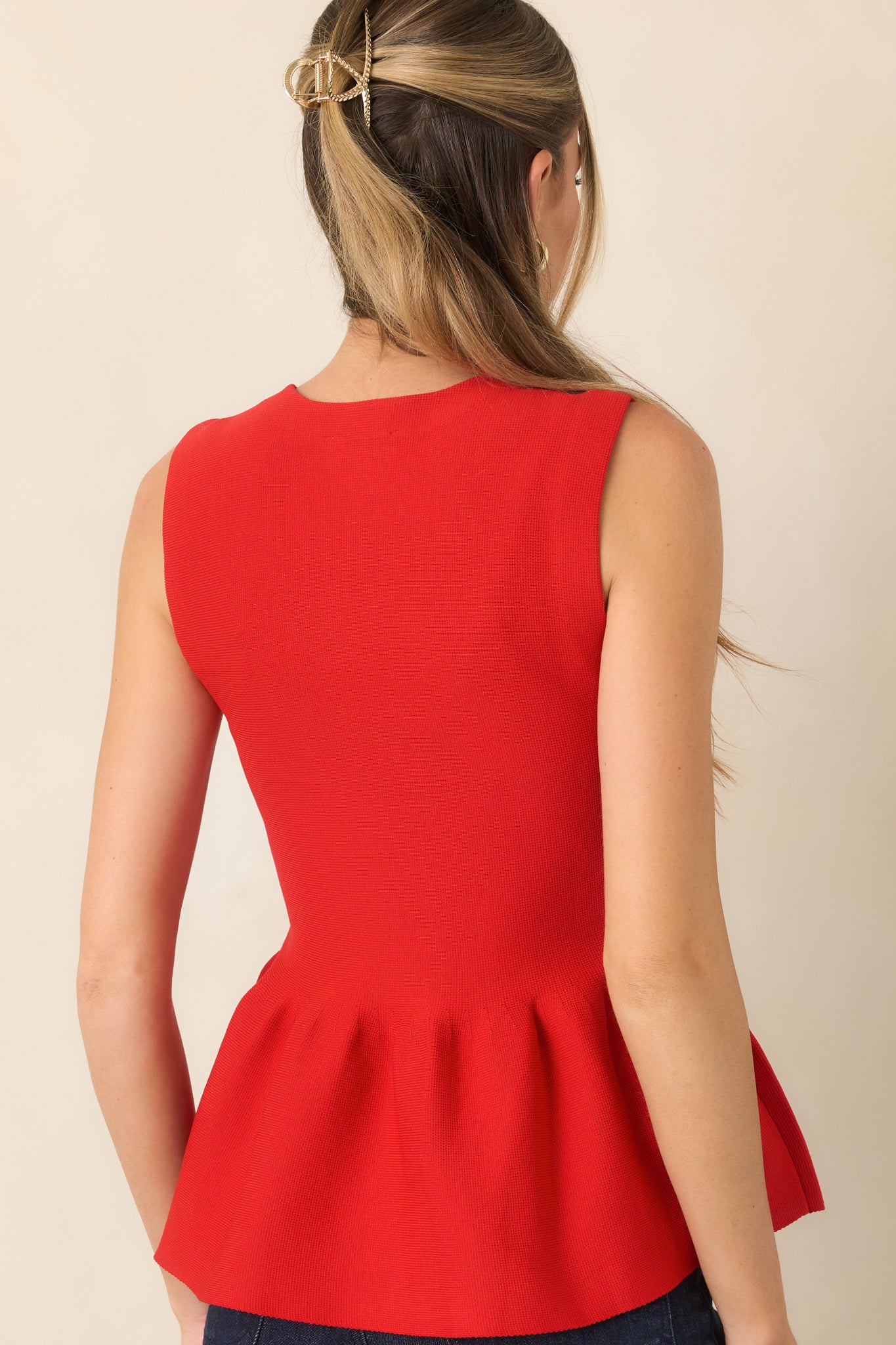 Rear view of the textured knit top displaying its sleeveless silhouette, structured shape, and softly flared peplum hem.