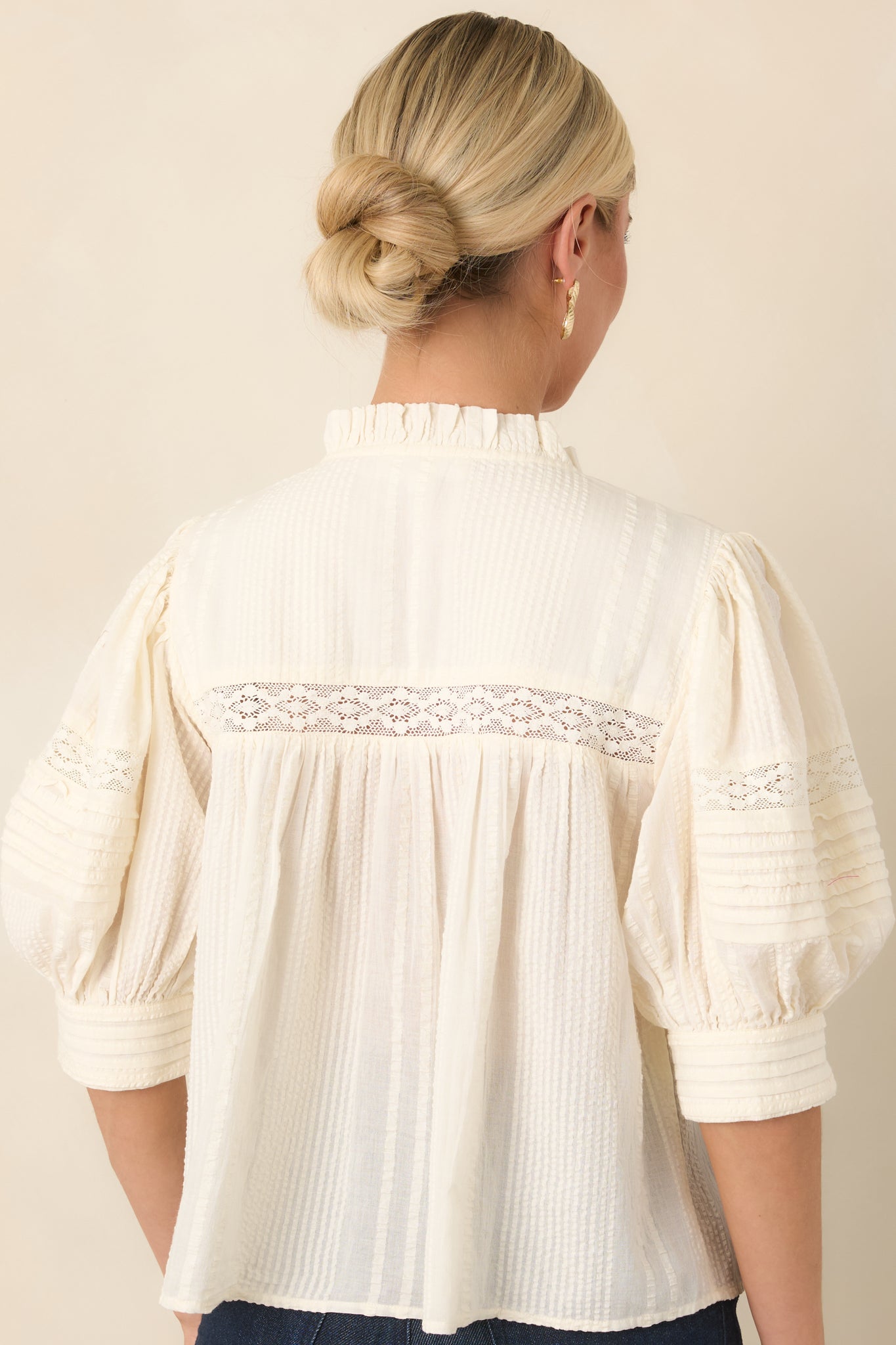 Rear view of the textured blouse showcasing its pleated fabric, softly gathered construction, and three-quarter balloon sleeves with lace accents.