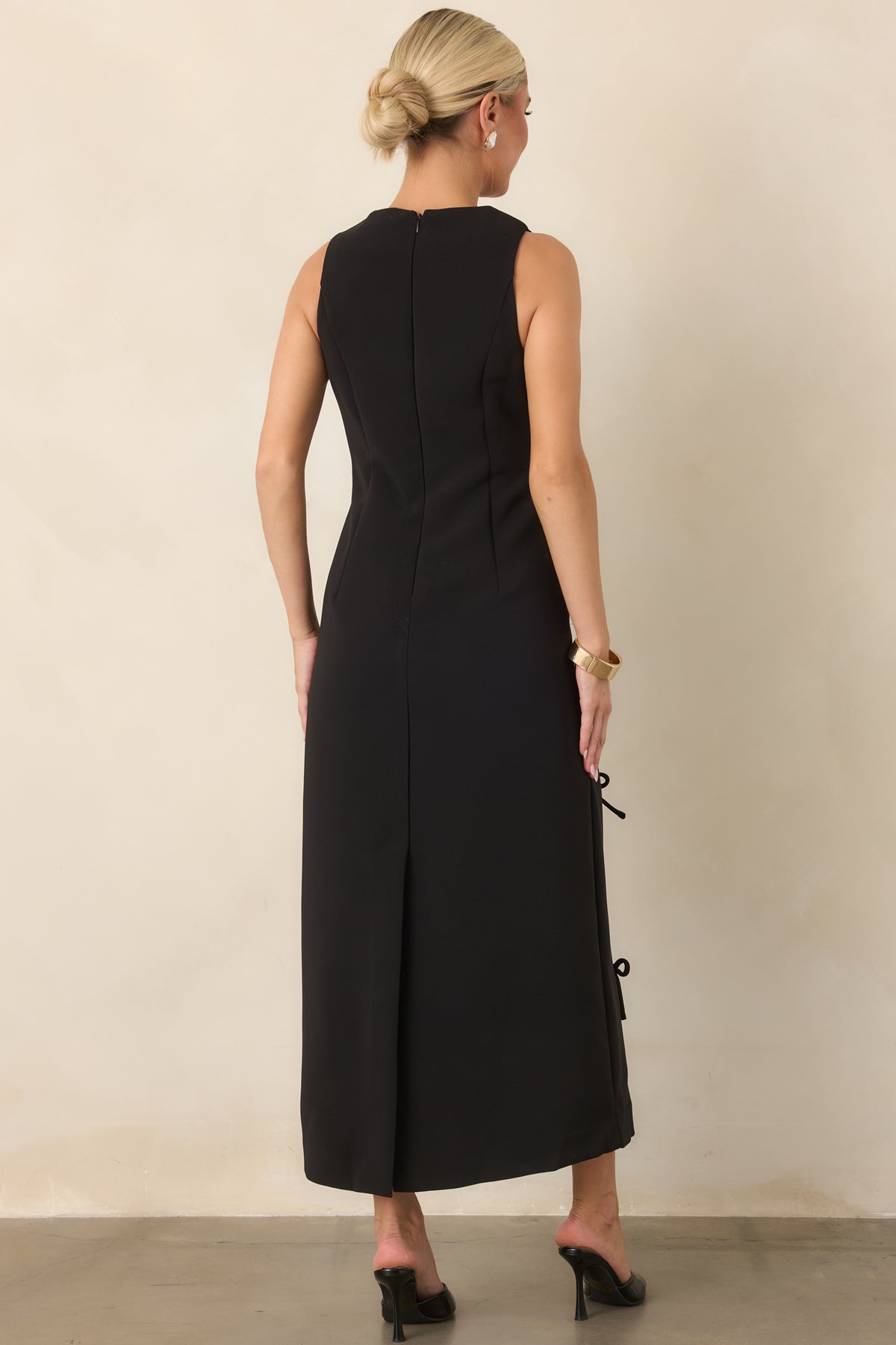 Rear view of the sleeveless maxi dress showing the tonal bow detailing, concealed back zipper, rear slit, and streamlined column silhouette.