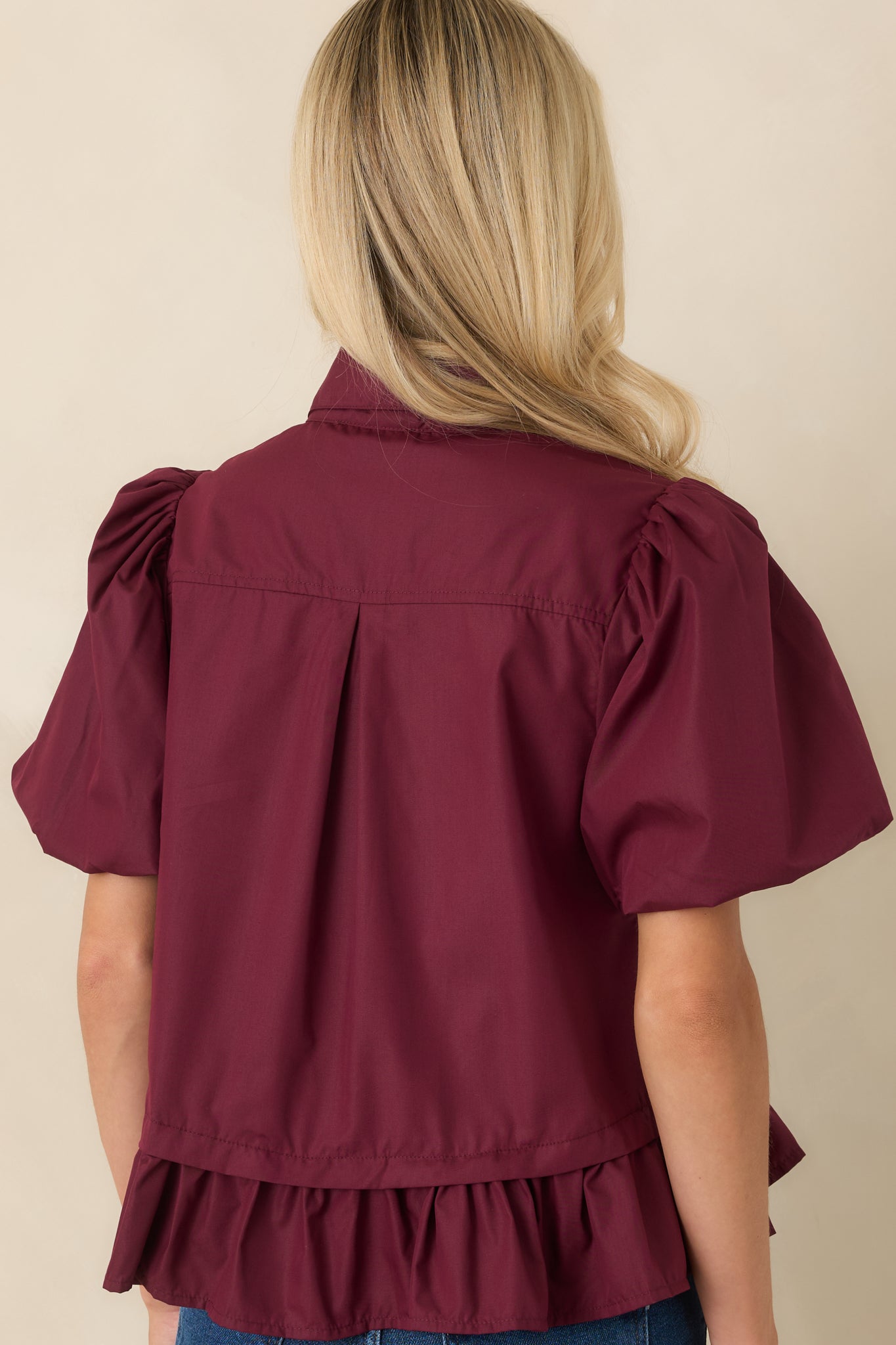Rear view of the wine red top highlighting the puff sleeves, flounced peplum hem, and smooth back design.