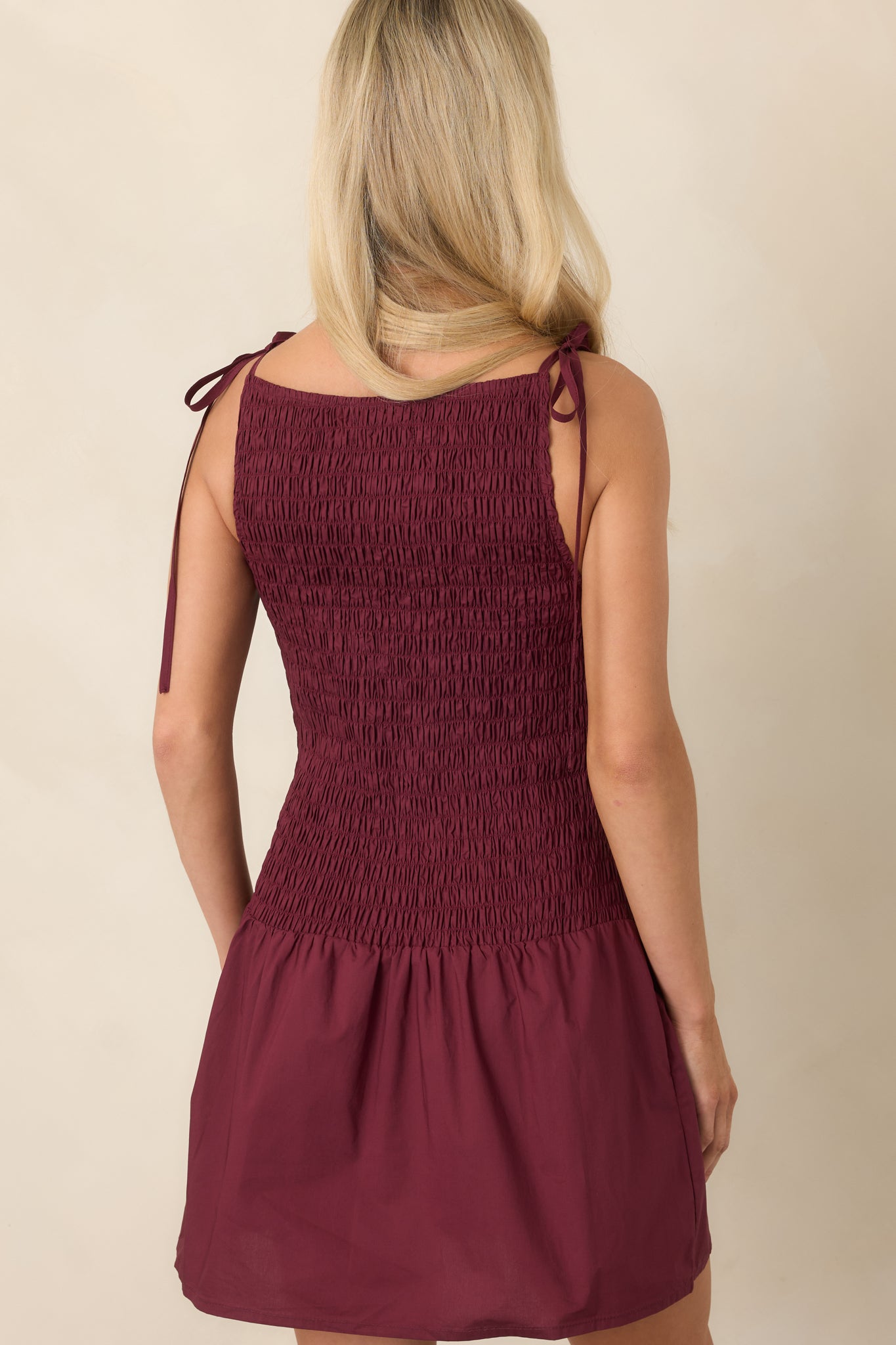 Rear view of the wine red cotton mini dress showcasing the shirred bodice, adjustable tie straps, gathered skirt, and softly flared hem.