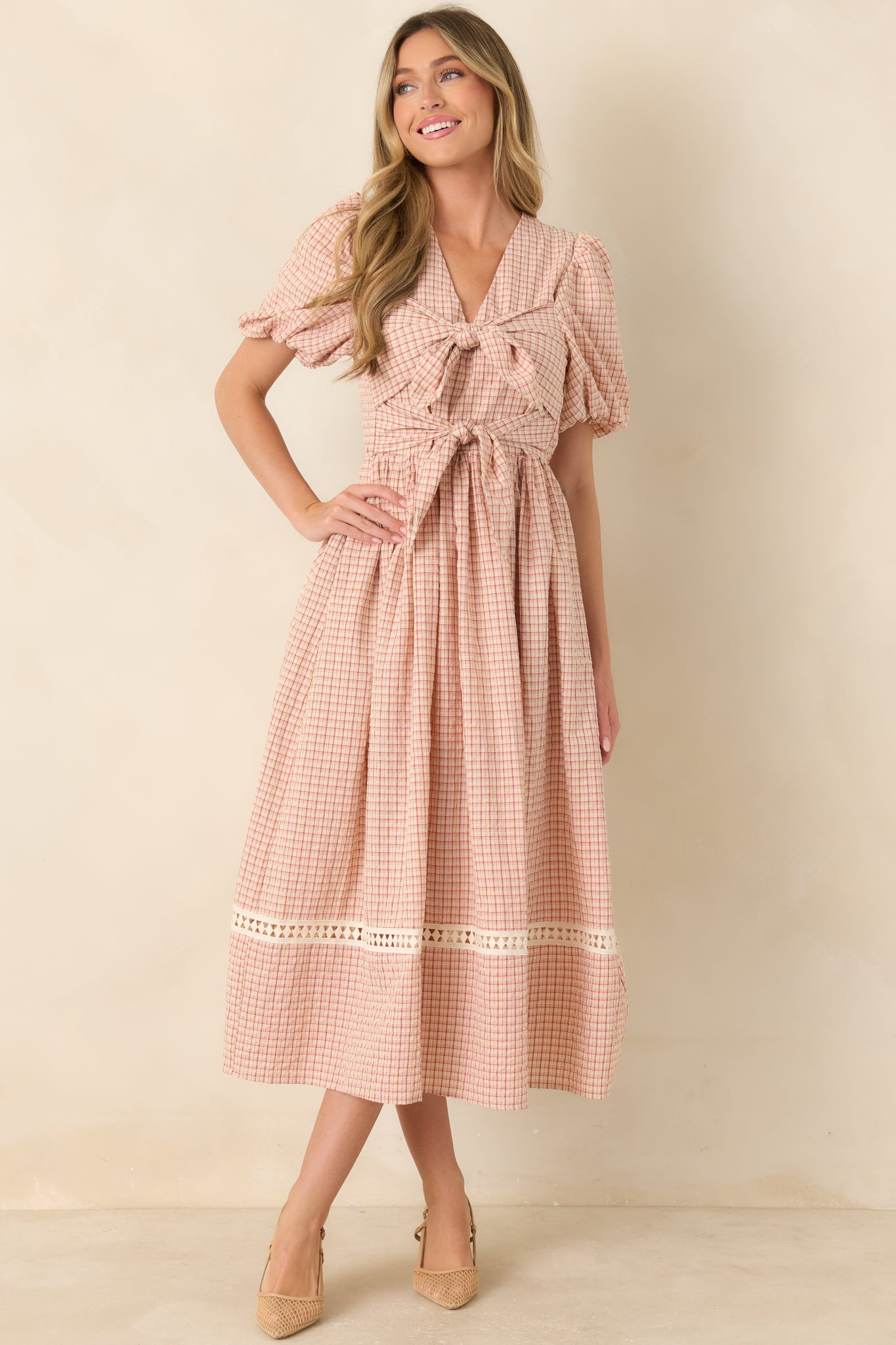 Red and beige plaid midi dress featuring a fitted bodice, puff sleeves, elastic waist, and full flowing skirt with oversized double ties at the front.