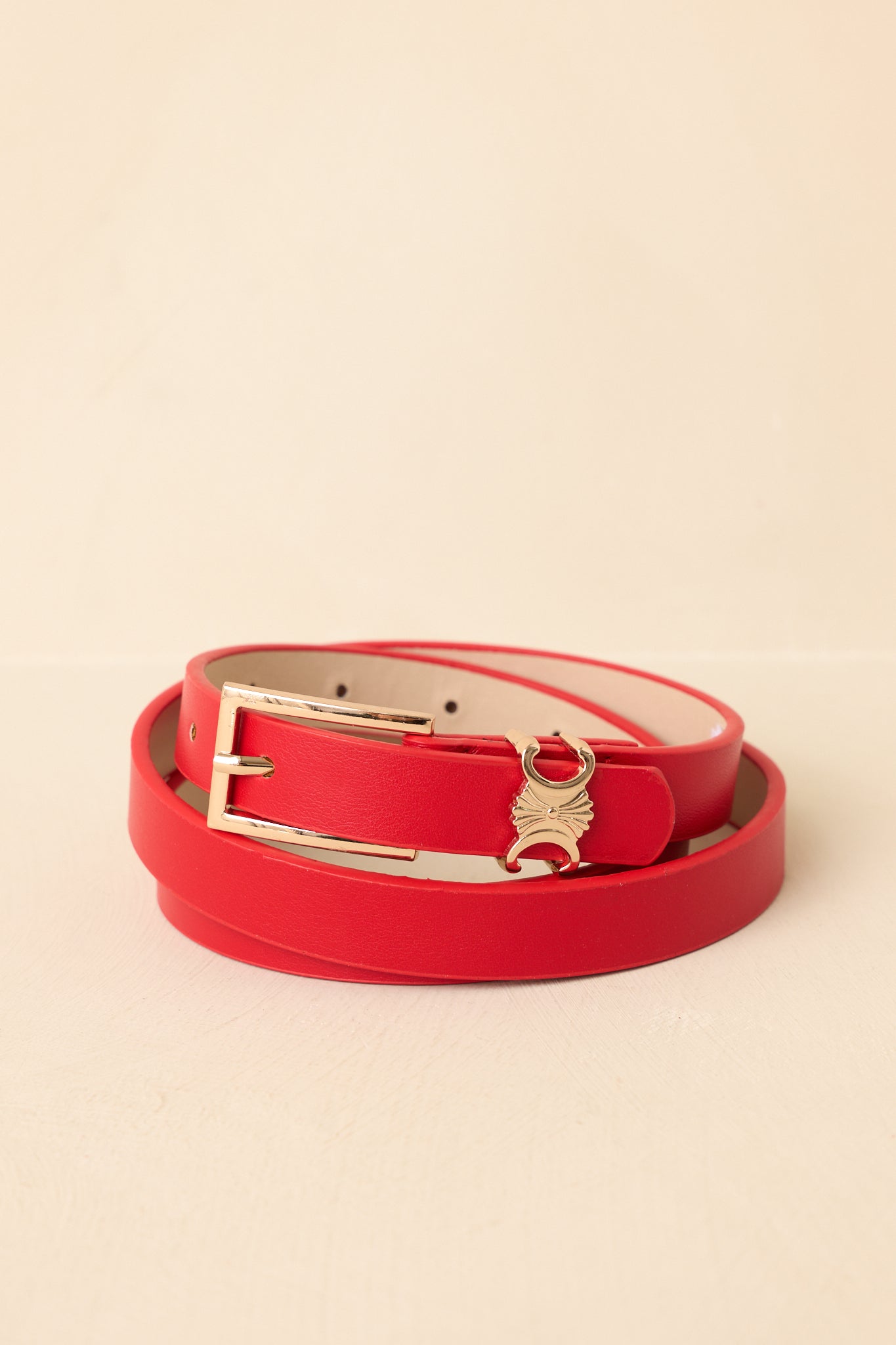 Red belt with a gold buckle on a beige background.