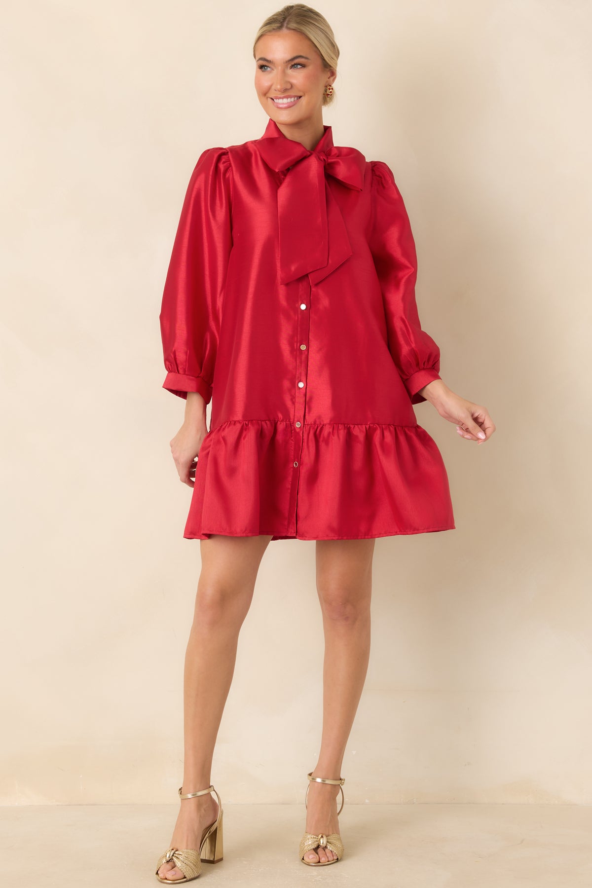 Red mini dress showcasing a statement bow neckline, functional gold-tone buttons, and a softly flared skirt.