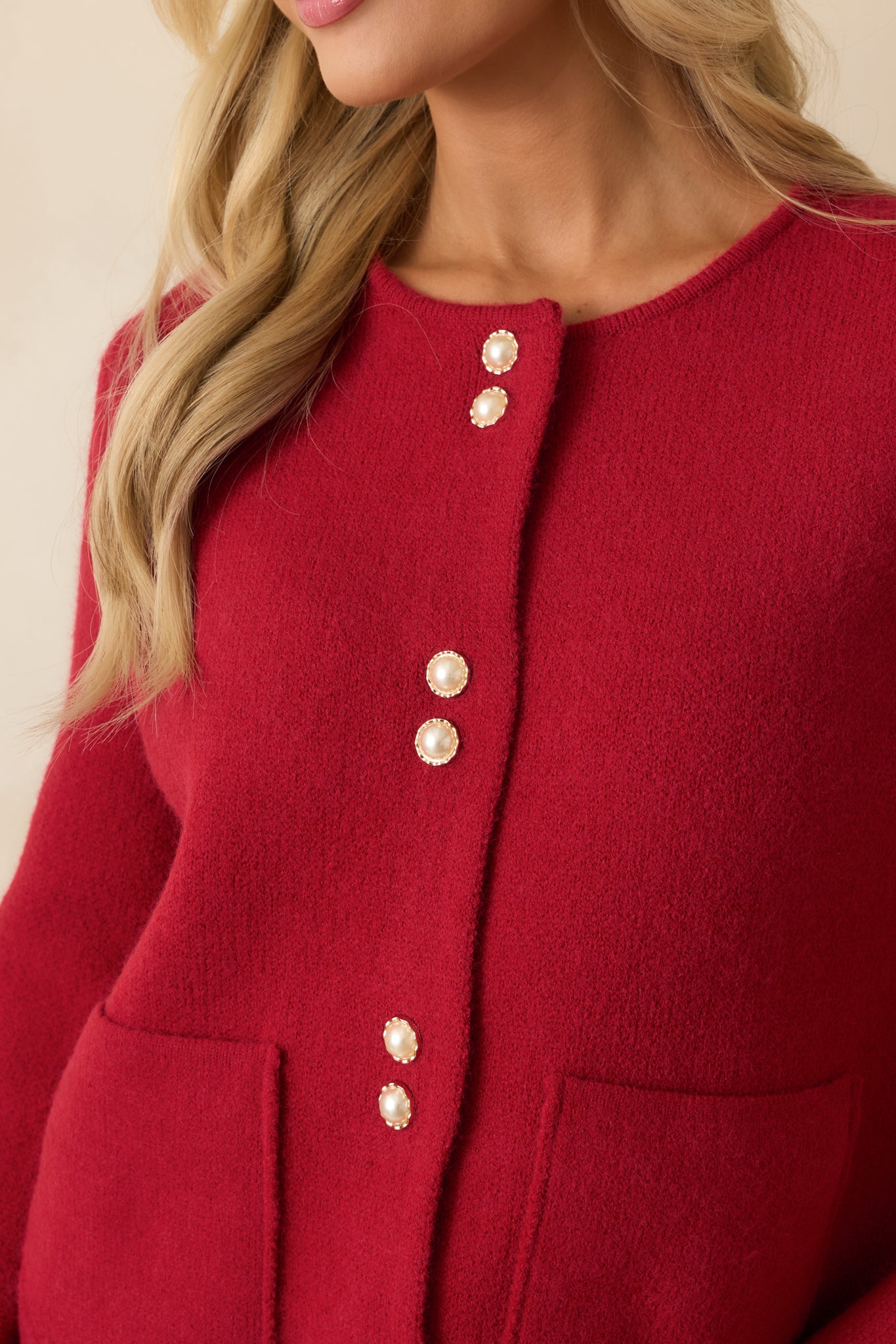 Detailed shot of the red cardigan showing the pearl-accent buttons, patch pockets, and textured knit fabric.