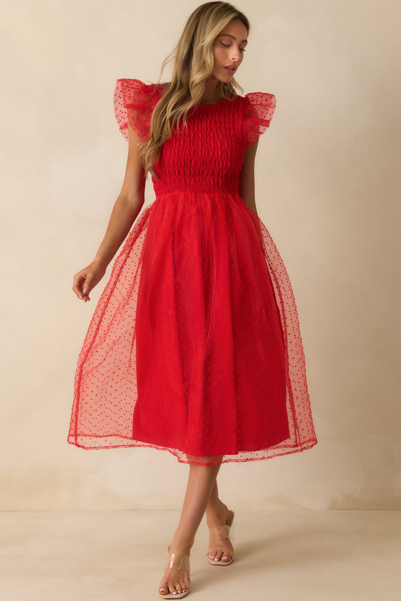Red dress with smocked bodice, flutter sleeves, and polka dot tulle overlay flowing into a lightweight silhouette.