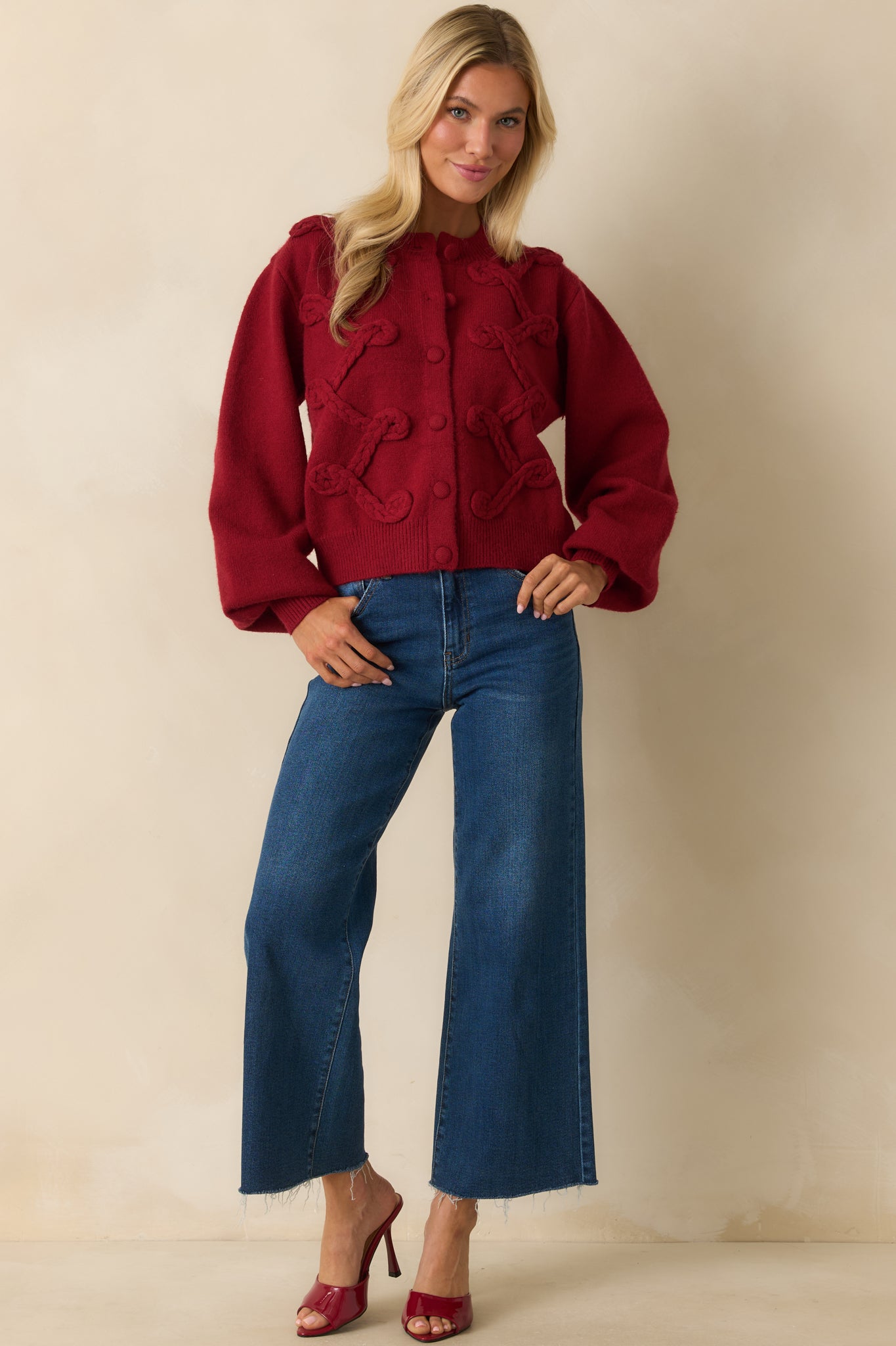 Red knit cardigan with thick braided appliqué across the front, long sleeves, round neckline, and front buttons.