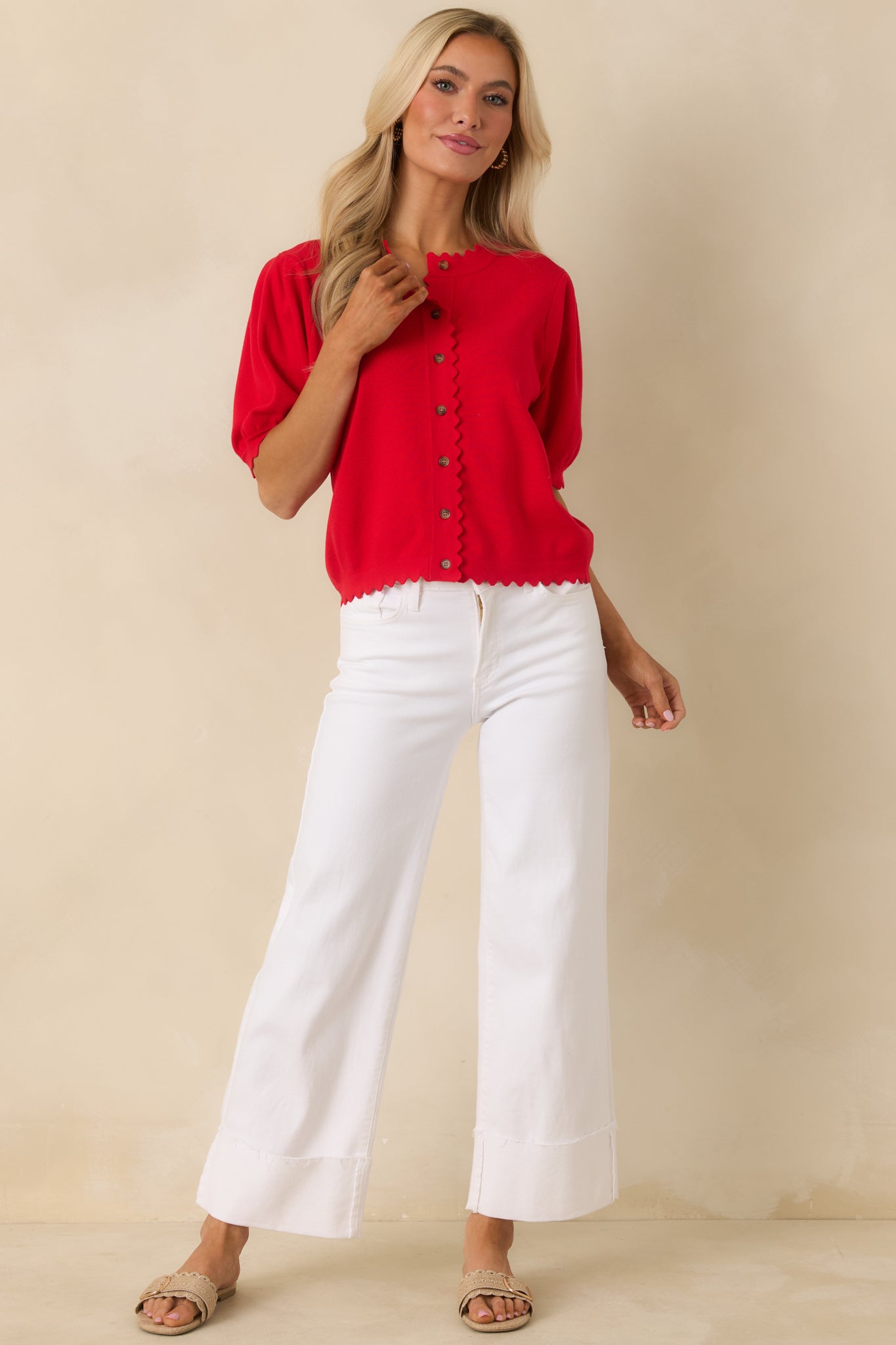 Front view of a red knit cardigan with a round neckline, short puff sleeves, and button-up front with scalloped edging.