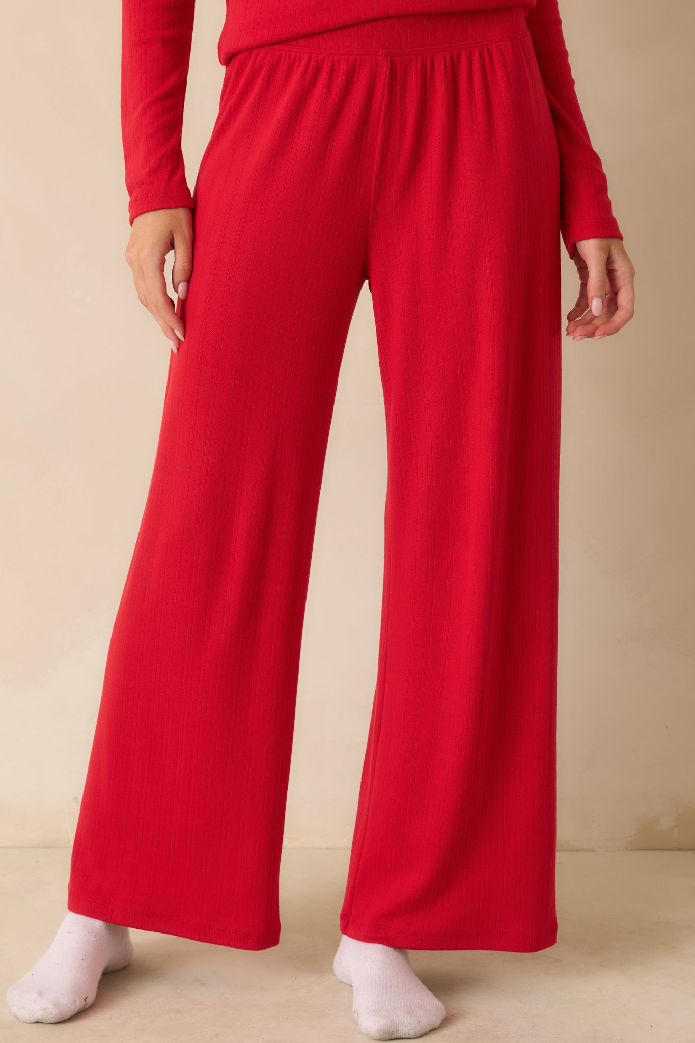 Detail of the front of red pointelle knit pants, emphasizing the high-rise waistband and smooth finish.