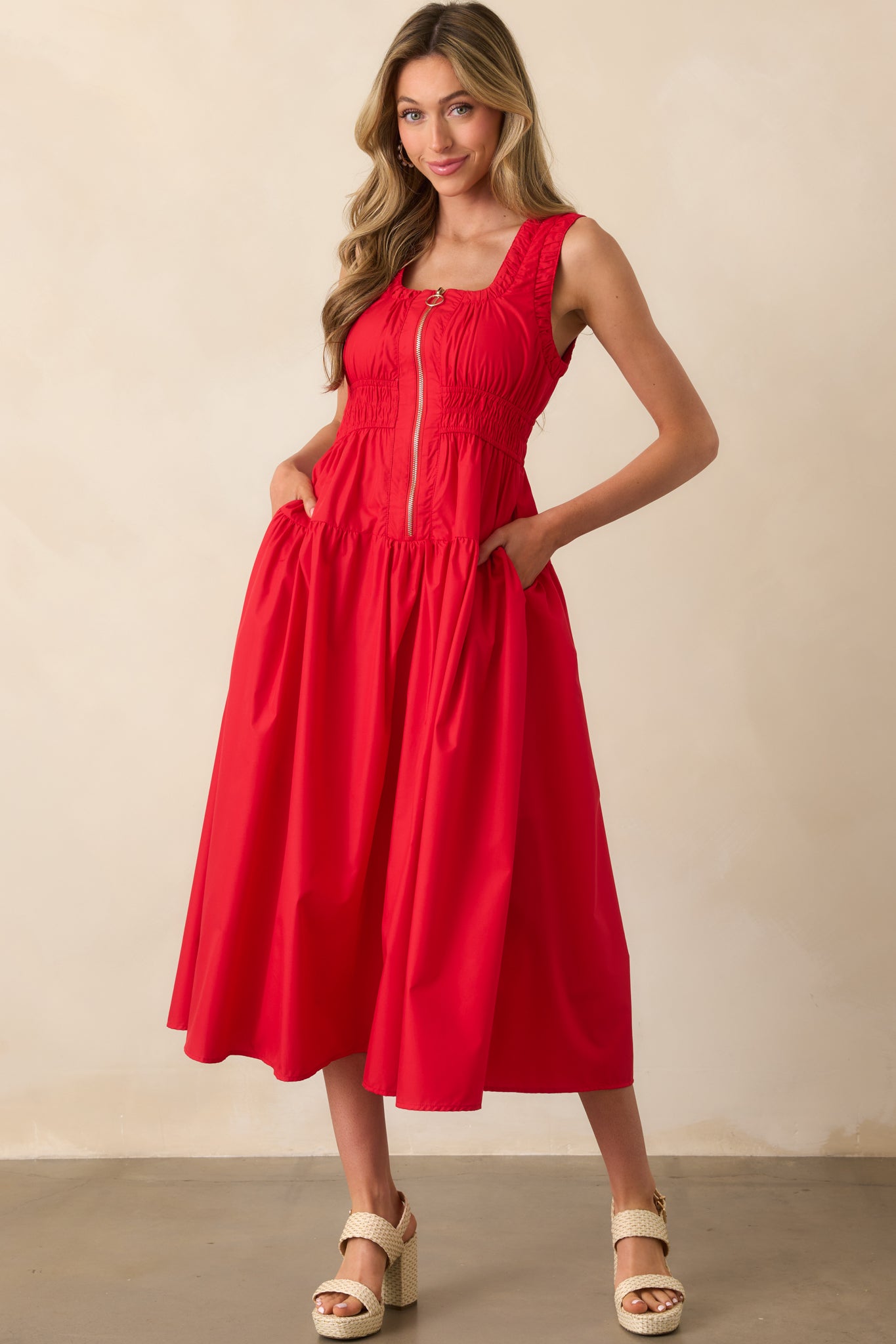 Front-facing image of a red midi dress with visible ruched waistline and functional pockets on each side.