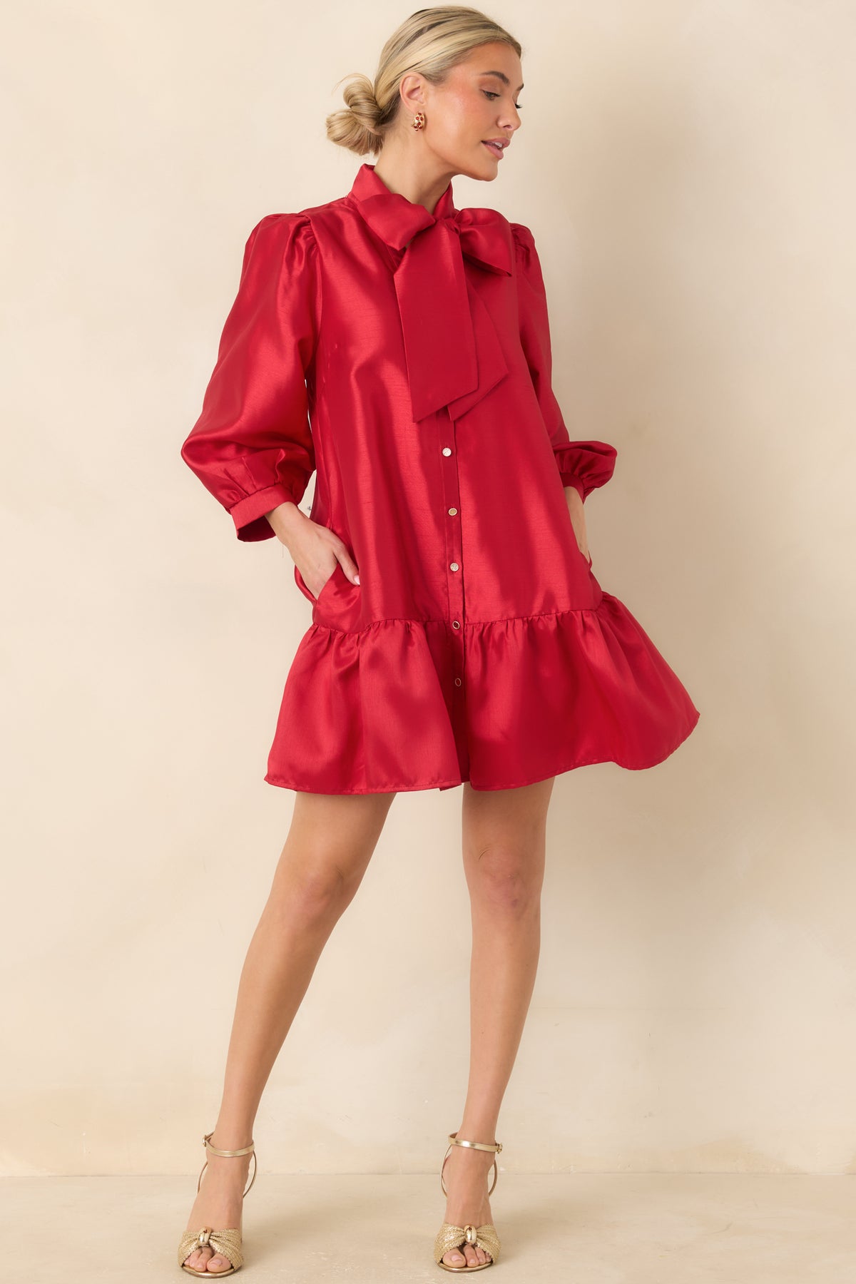 Red mini dress featuring an oversized neck tie bow, gold-tone front buttons, and three-quarter puff sleeves.