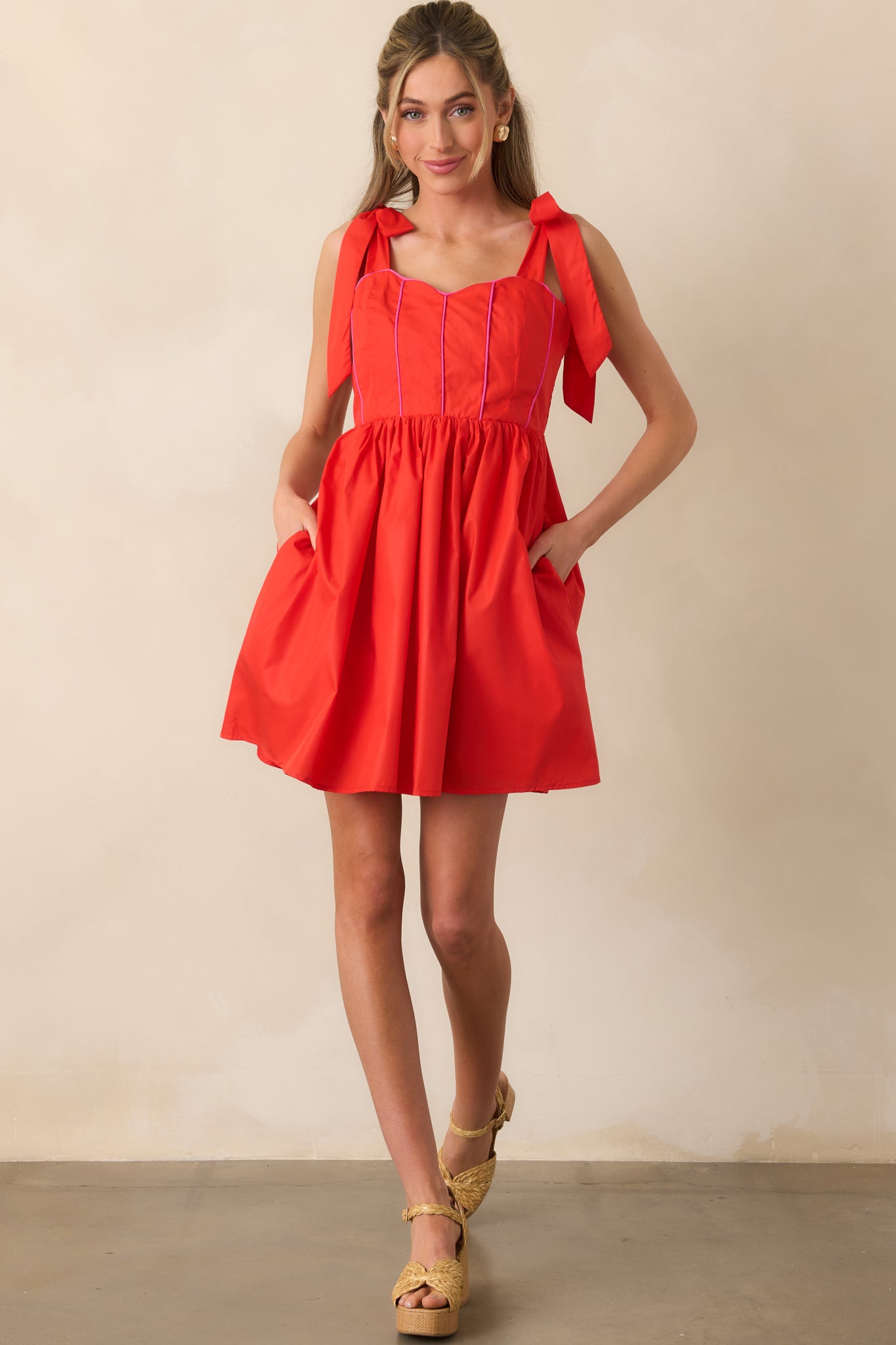 Red mini dress with sweetheart neckline and pink corset-style trim, shown with bow-tied shoulder straps and flared skirt.