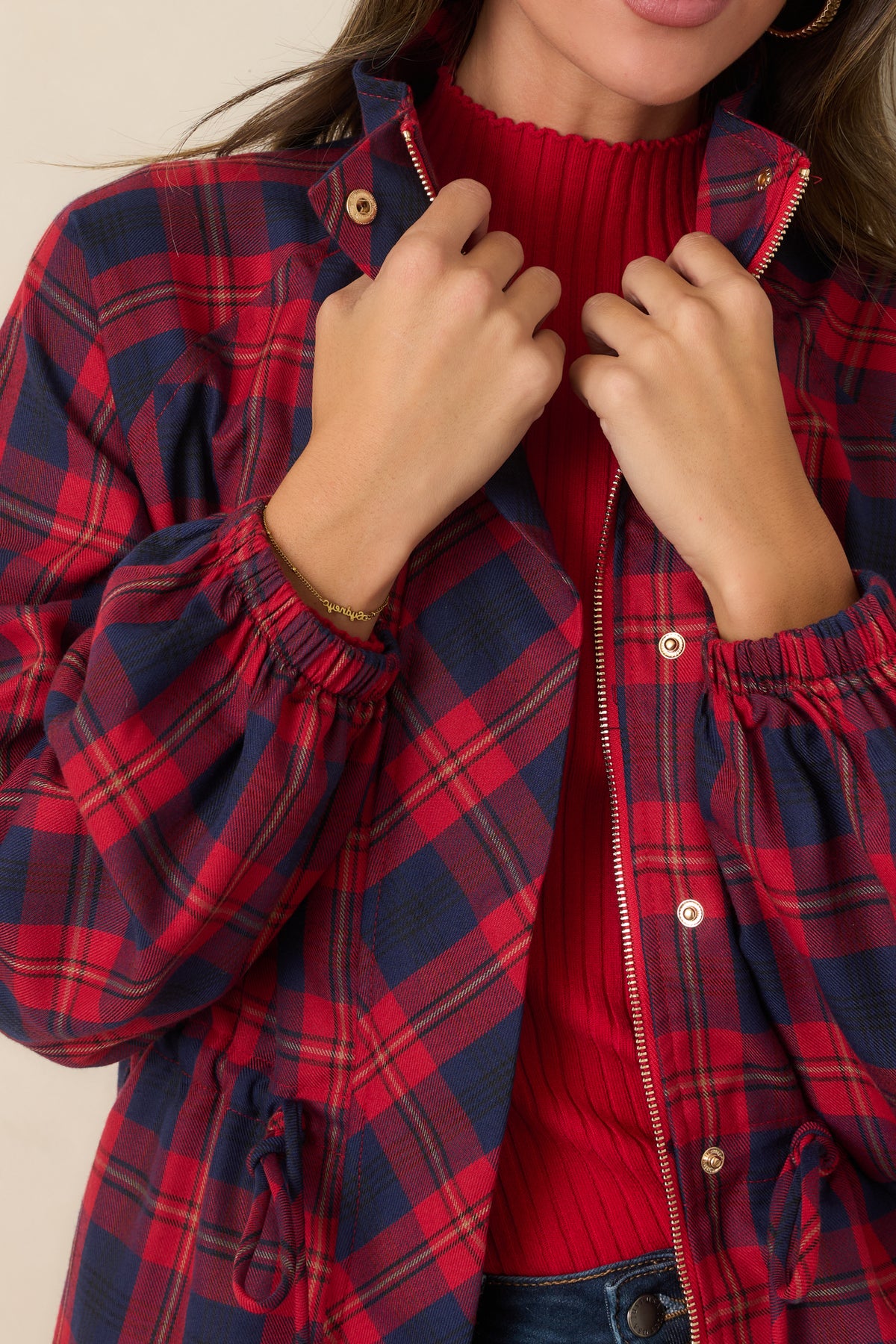 Close-up detail of the red and navy plaid jacket showing the zip-front closure, structured collar, and snap accents.