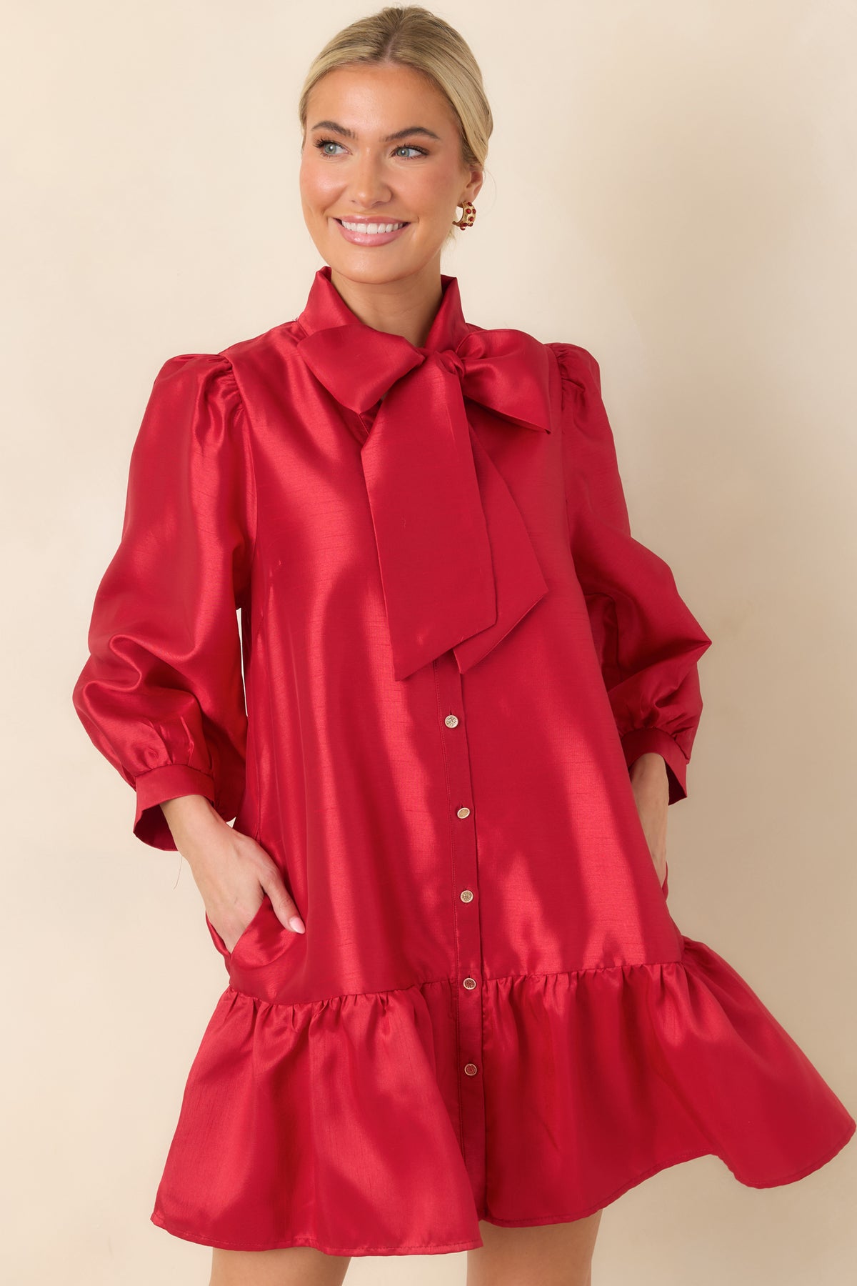 Red dress highlighting the oversized neck tie knotted into a statement bow above the gold-tone button front.