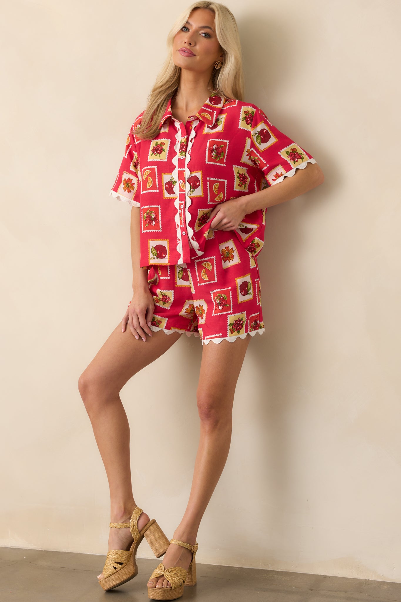 Red patchwork shorts with floral and fruit motifs shown full-length from the front, highlighting the pleated front and relaxed silhouette.